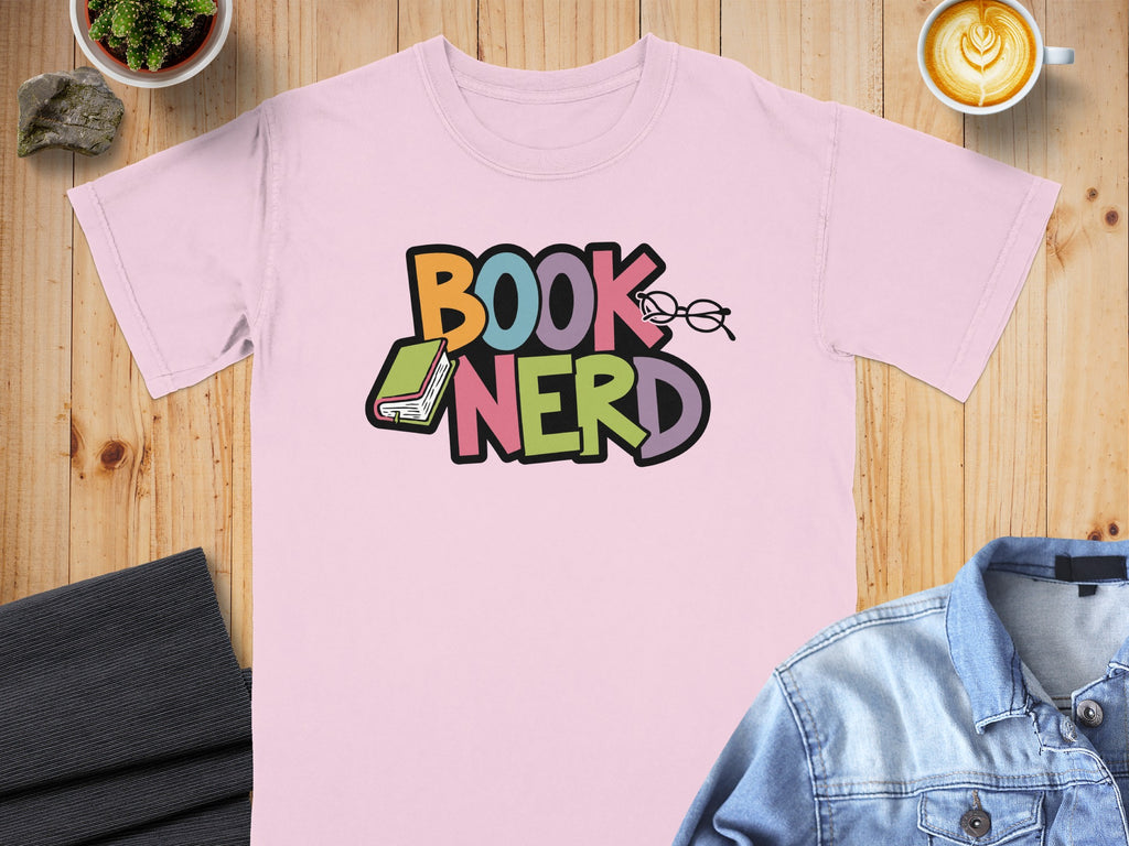 Pink t-shirt with colorful "BOOK NERD" text, a book, and glasses graphic.