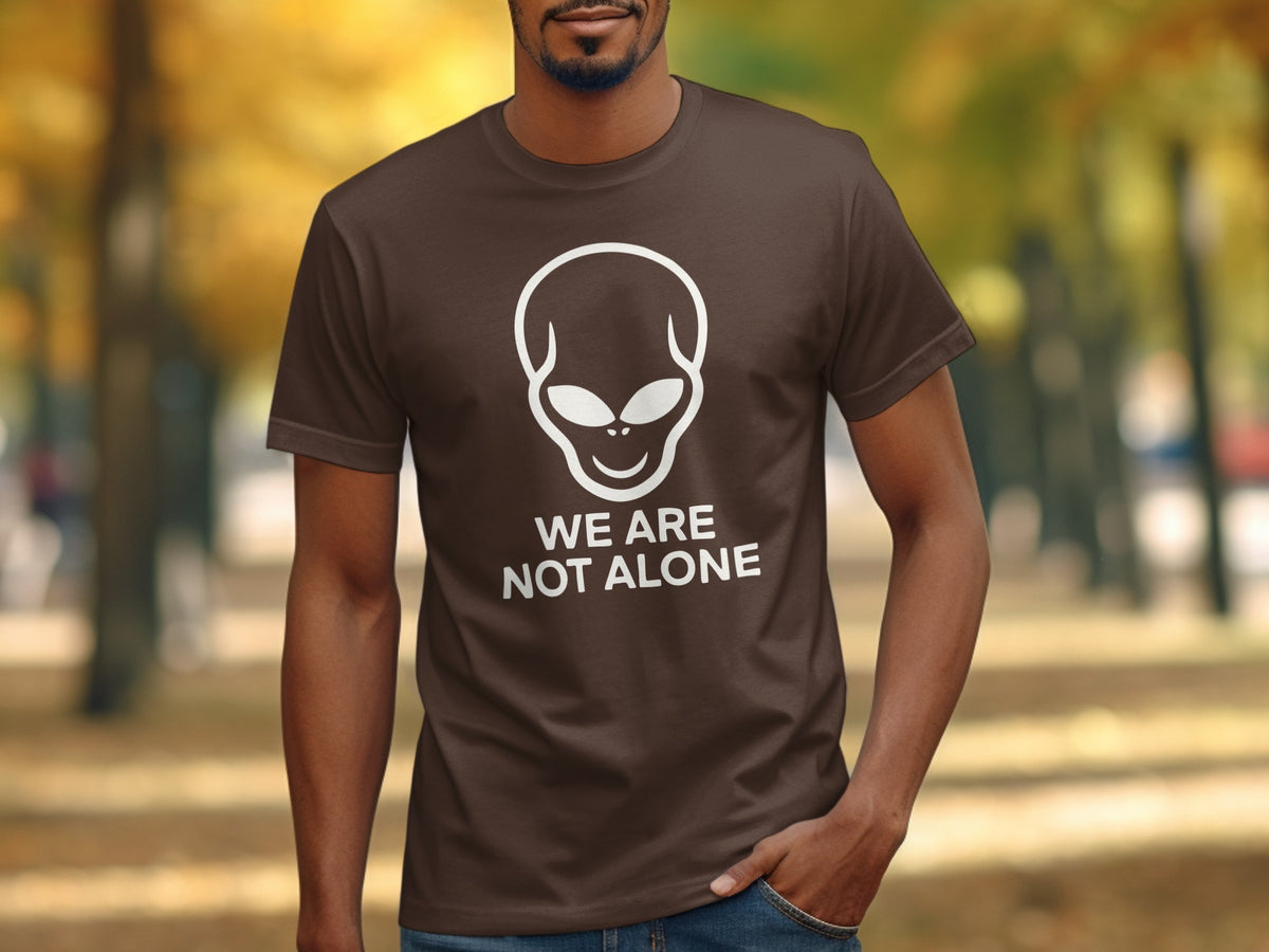 Brown t-shirt with white alien graphic and text "WE ARE NOT ALONE".