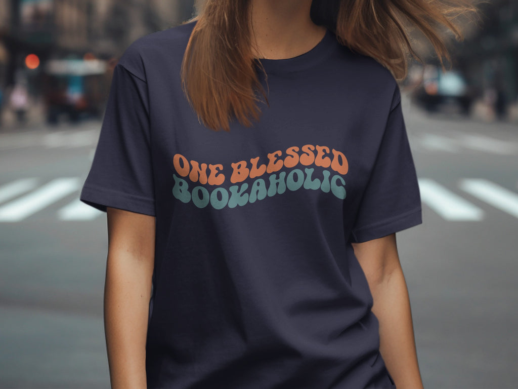 Navy t-shirt with retro text "ONE BLESSED BOOKAHOLIC" in orange and teal.