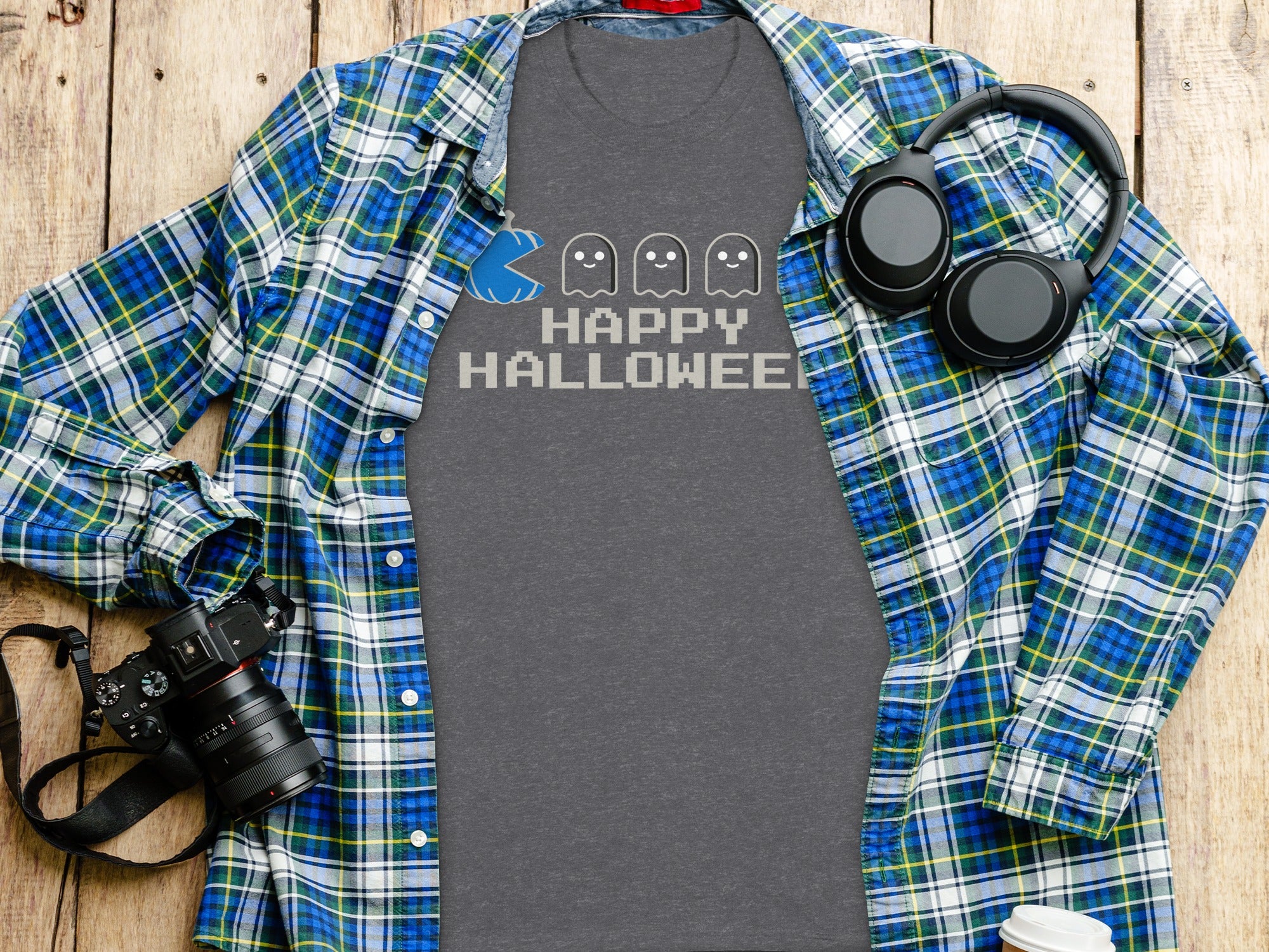 Grey t-shirt with "Happy Halloween" and pixelated ghosts, flat lay with plaid shirt.