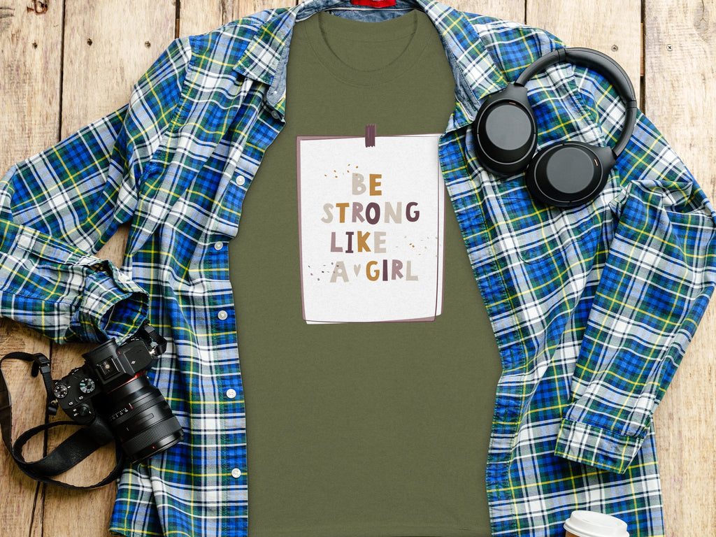 Green t-shirt with "Be Strong Like A Girl" graphic, plaid shirt, headphones, and camera.