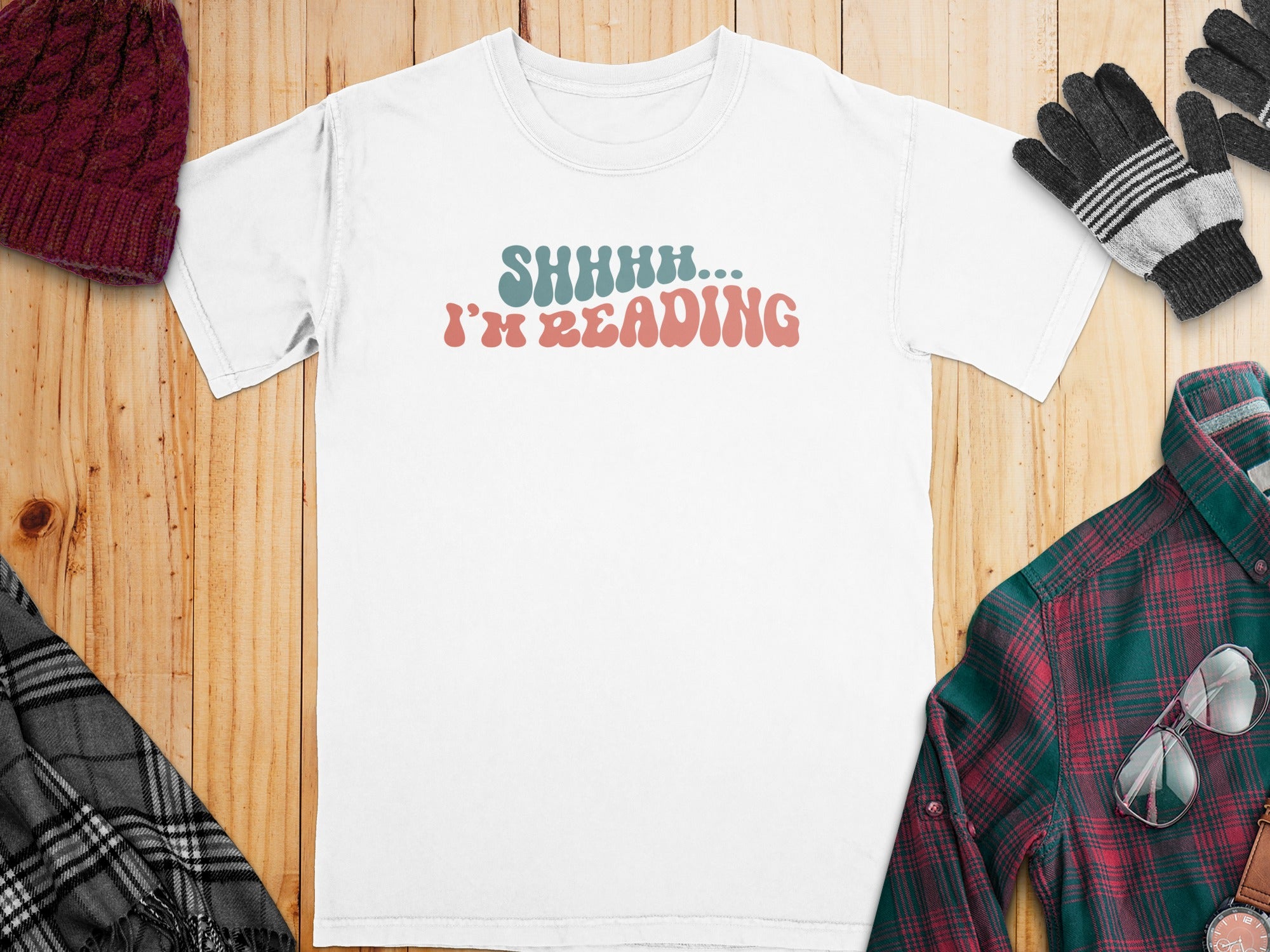 White t-shirt with "SHHHH... I'M READING" text, surrounded by winter accessories.