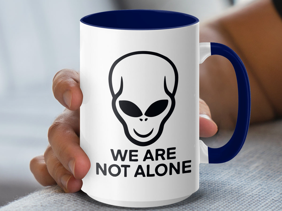 White mug with blue handle, featuring an alien head and "WE ARE NOT ALONE" text.