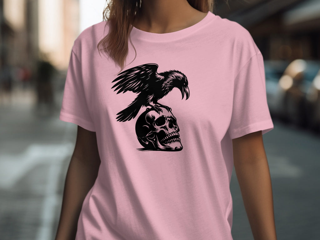 Black crow perched on a skull graphic on a pink t-shirt.