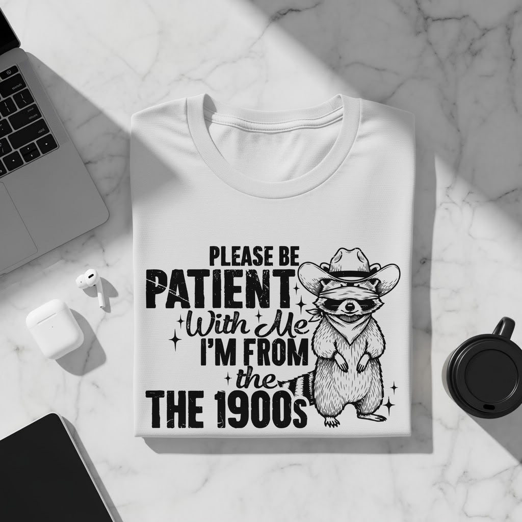 White t-shirt with raccoon graphic and text "Please be patient with me I'm from the 1900s".