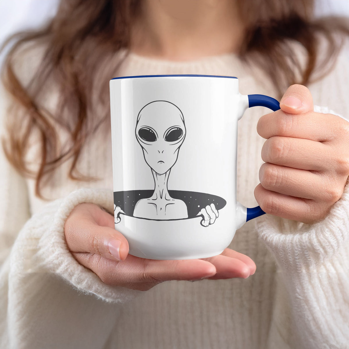 White mug with blue rim and handle, featuring a line drawing of an alien peeking out.