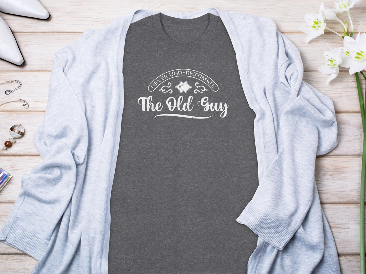 Dark gray t-shirt with white text "Never Underestimate The Old Guy."
