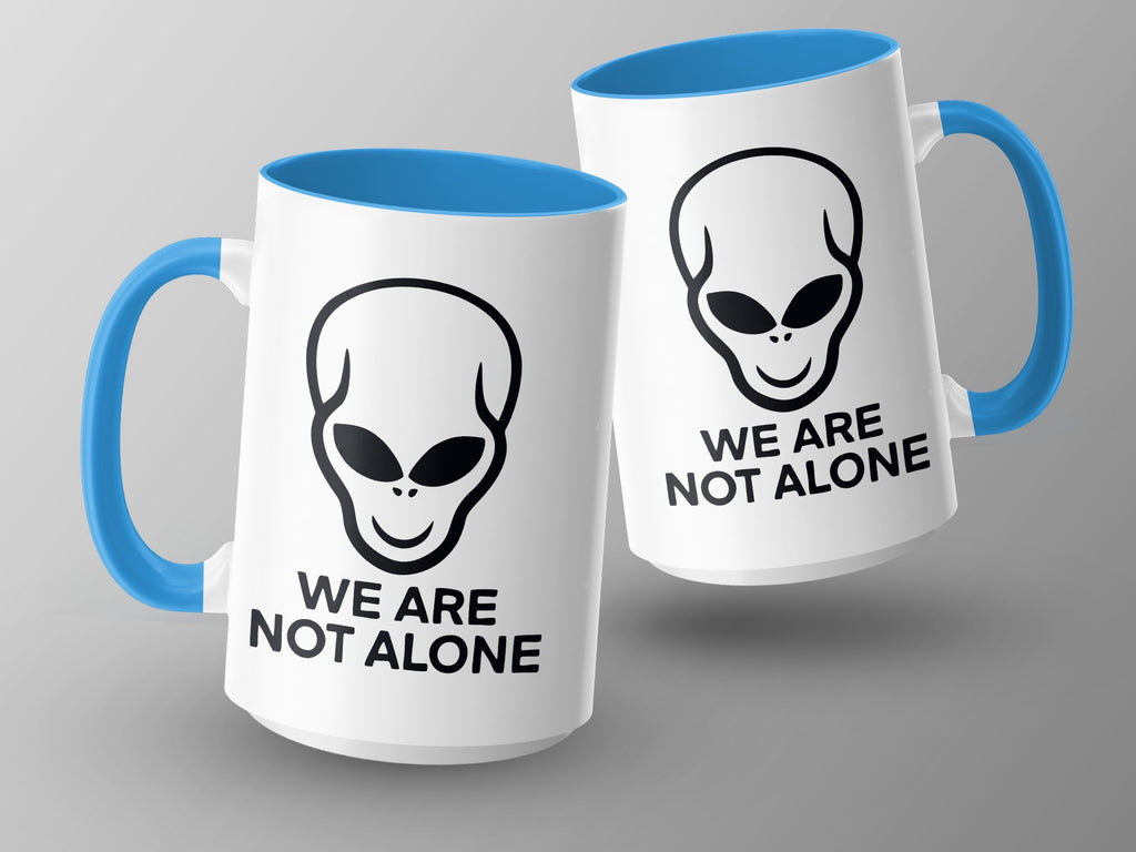 Two white mugs with blue handles and interiors, featuring alien heads and "We Are Not Alone" text.