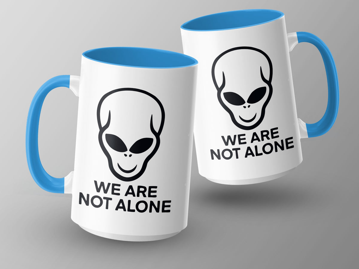 Two white mugs with blue handles and interiors, featuring alien heads and "We Are Not Alone" text.