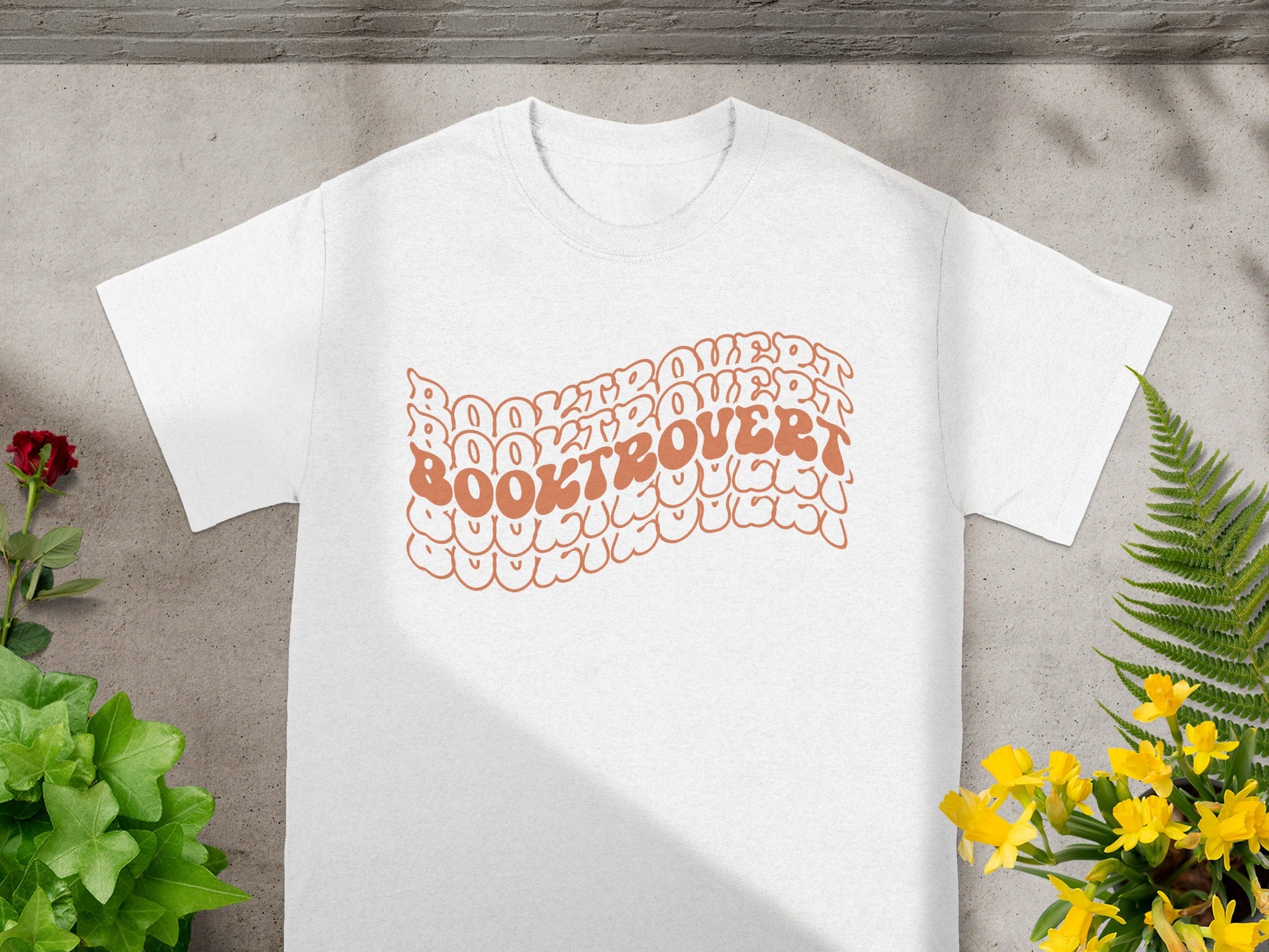 White t-shirt with brown text reading "BOOKTROVERT" in wavy, bubble-like font.