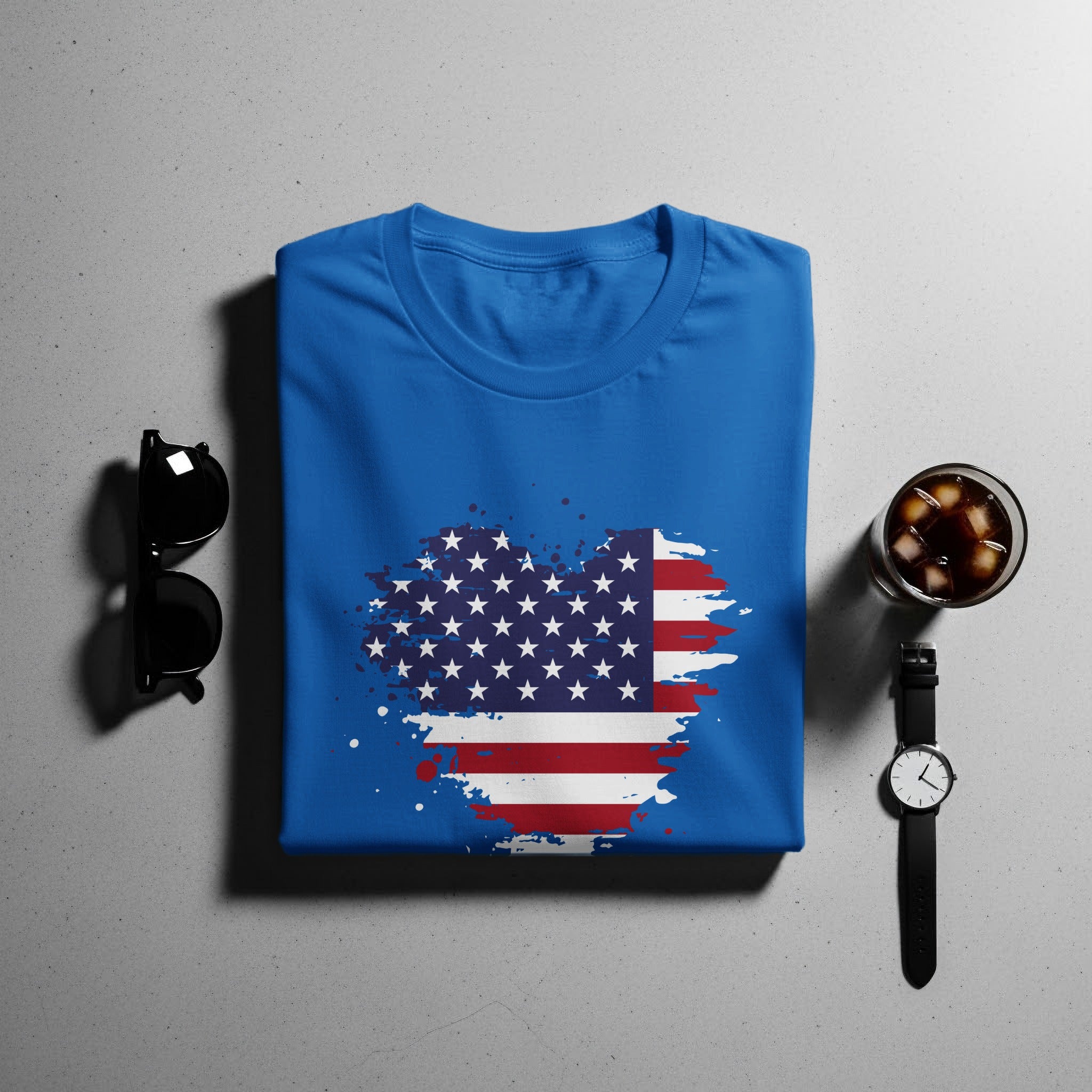 Blue t-shirt with a distressed American flag graphic, sunglasses, drink, and watch.