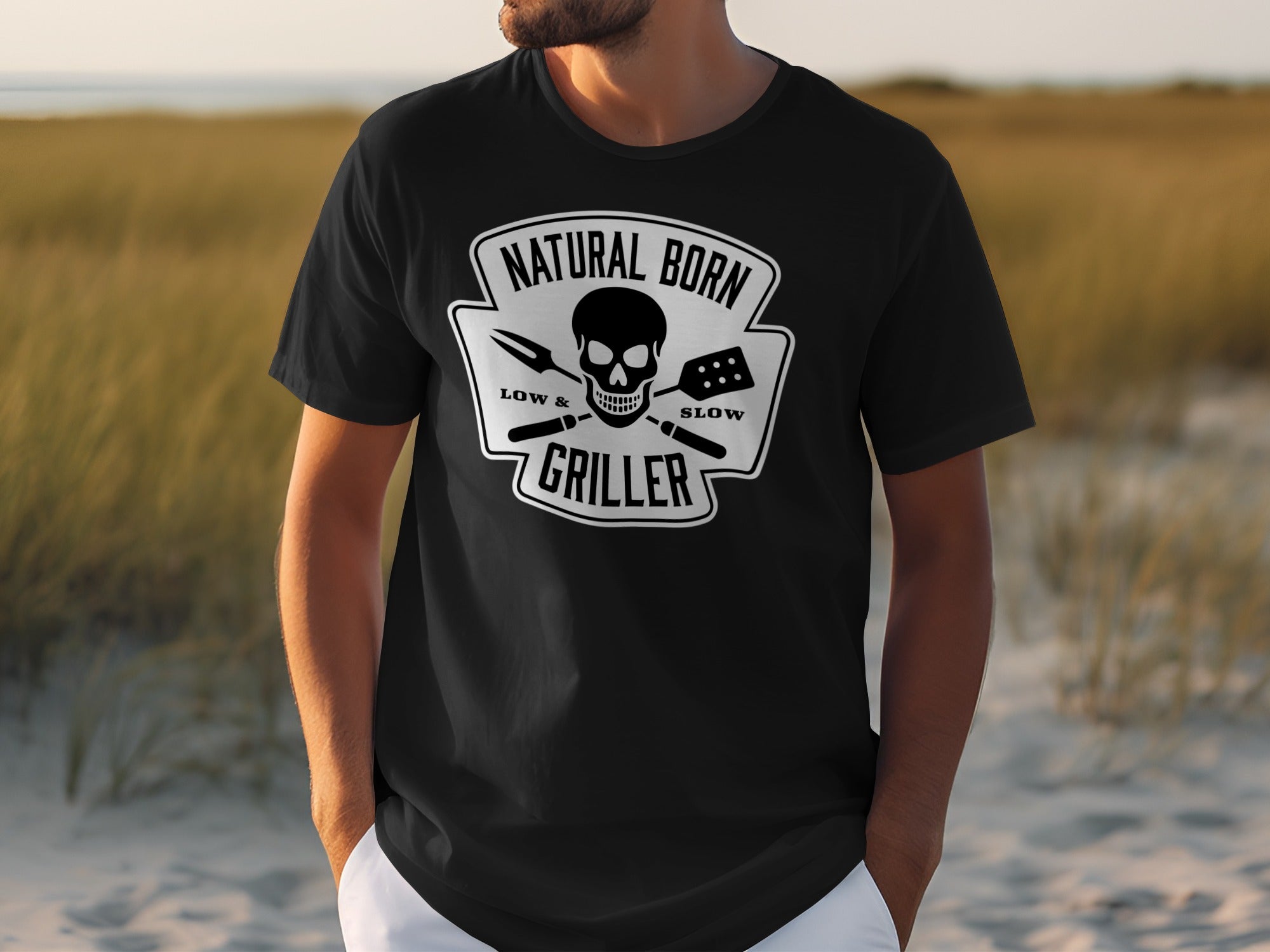 Black t-shirt with "NATURAL BORN GRILLER" text, skull, and BBQ tools design.