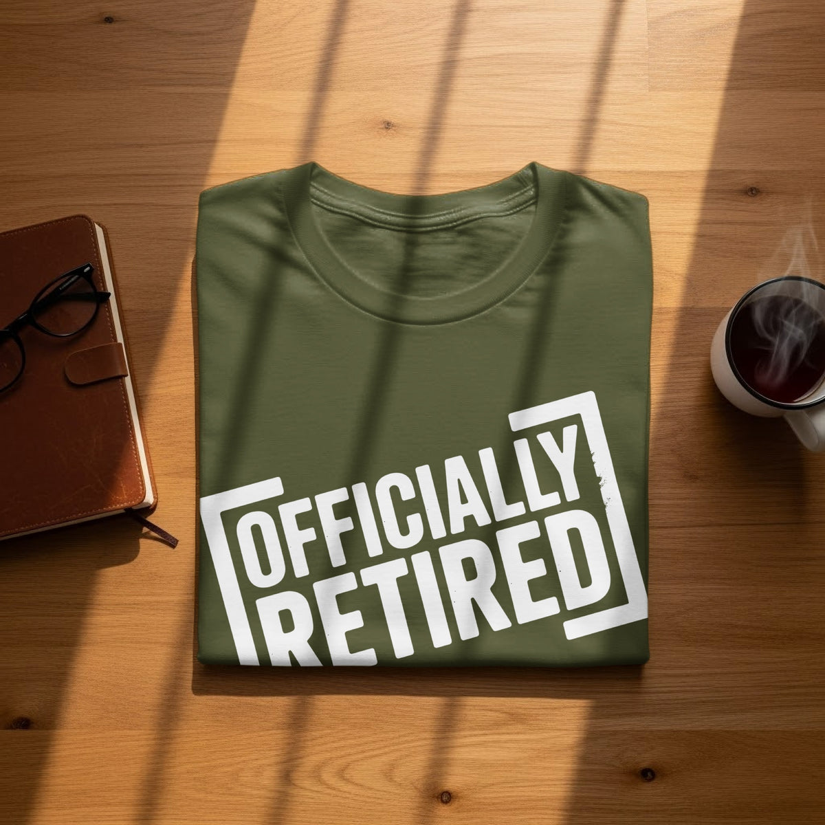 Green t-shirt with white text "OFFICIALLY RETIRED" on a wooden surface.