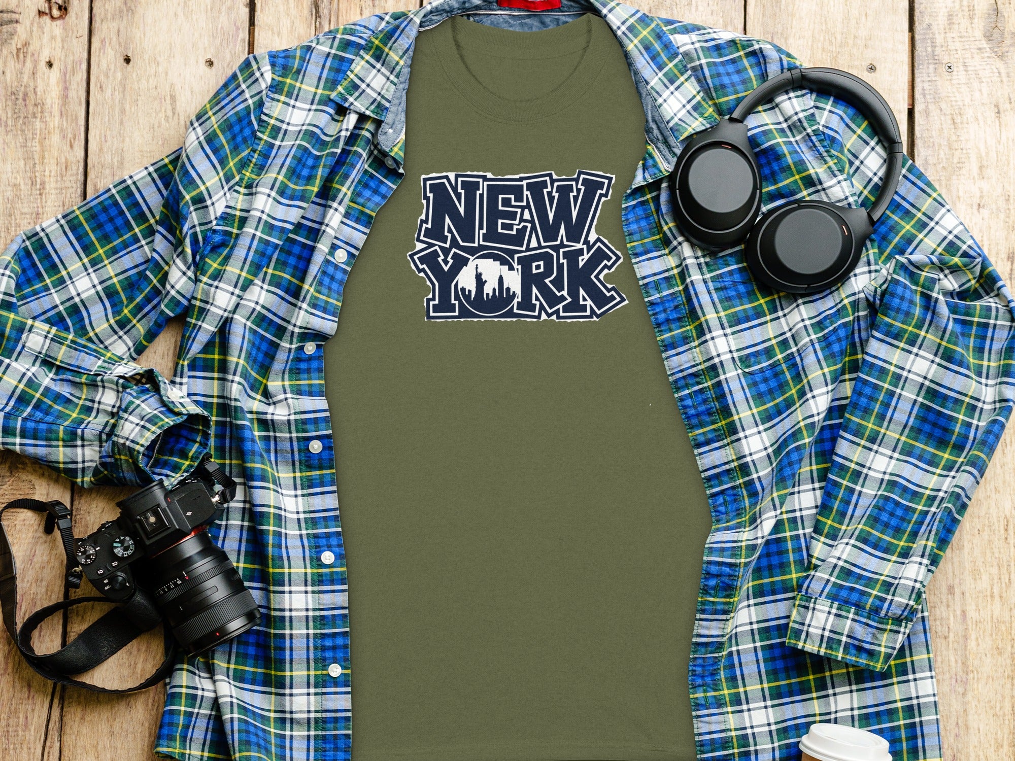 Olive green t-shirt with "New York" skyline graphic, over blue plaid shirt.