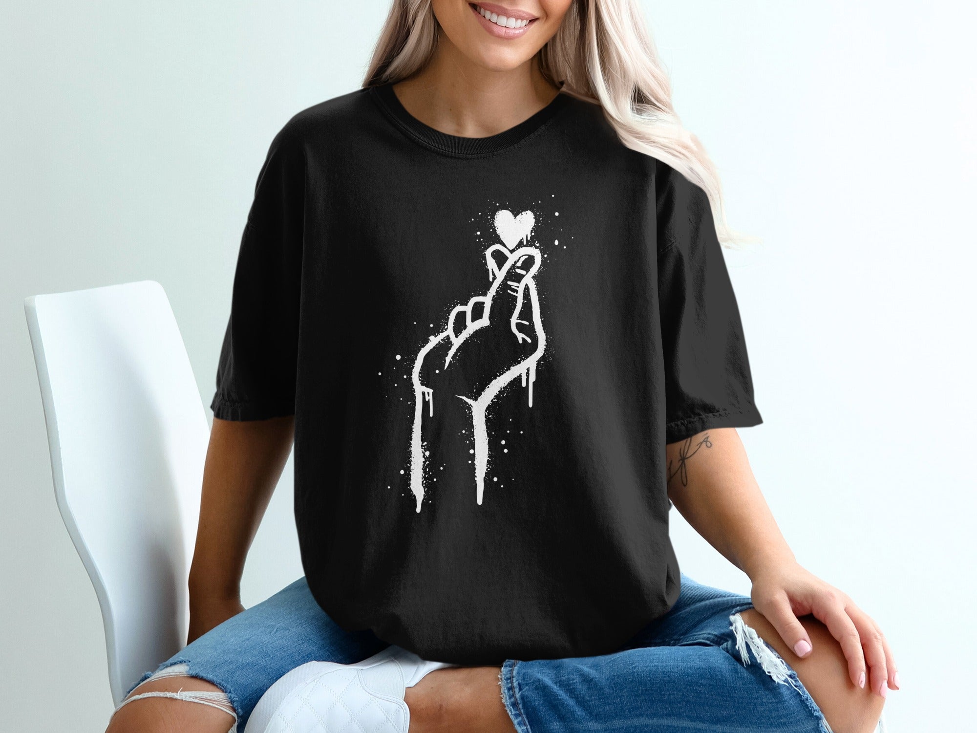 Black t-shirt with white graphic of hand making heart shape with dripping effect.