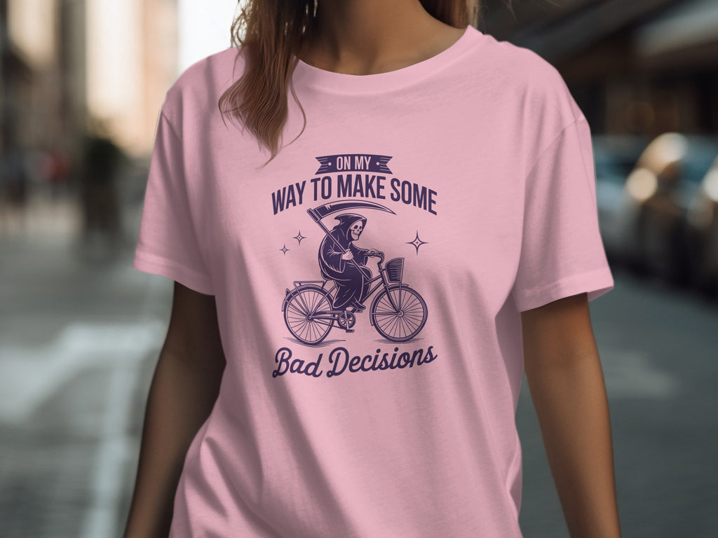 Pink t-shirt with a dark purple graphic of the Grim Reaper on a bicycle and text "On My Way To Make Some Bad Decisions".