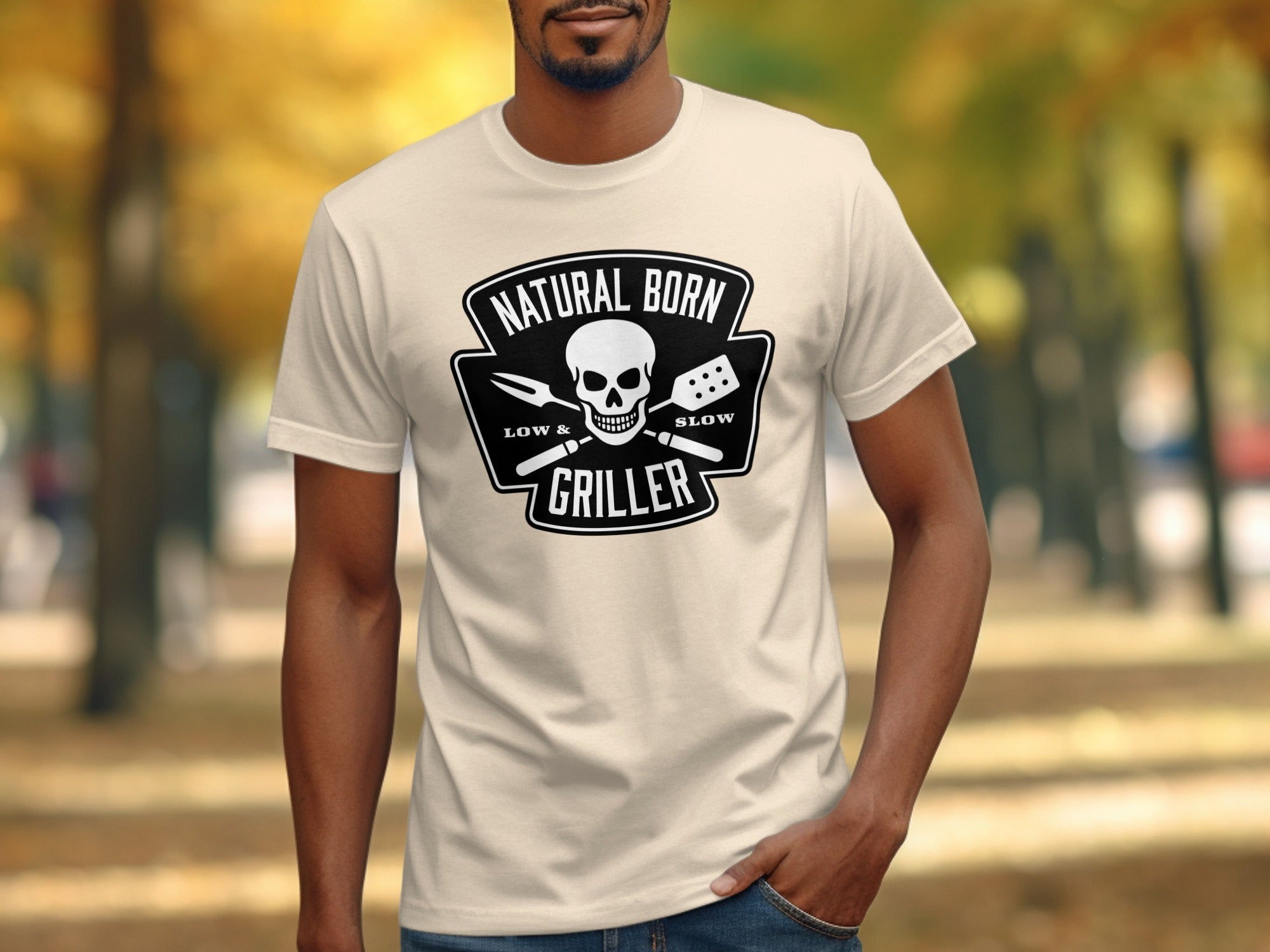 Cream t-shirt with black graphic of skull, fork, and spatula reading "Natural Born Griller".