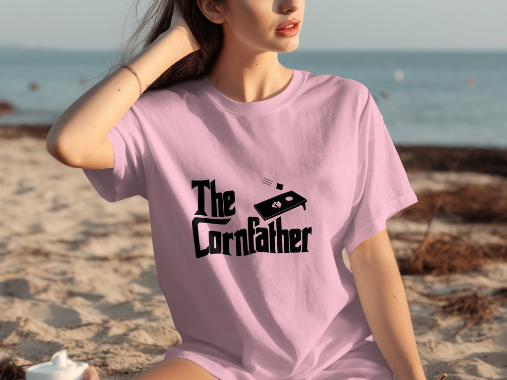 Pink t-shirt with "The Cornfather" and cornhole board graphic on the front.
