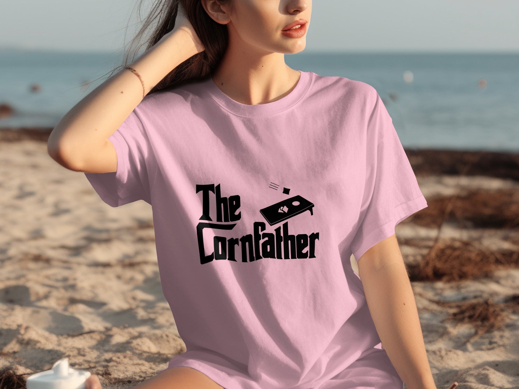 Pink t-shirt with "The Cornfather" and cornhole board graphic on the front.