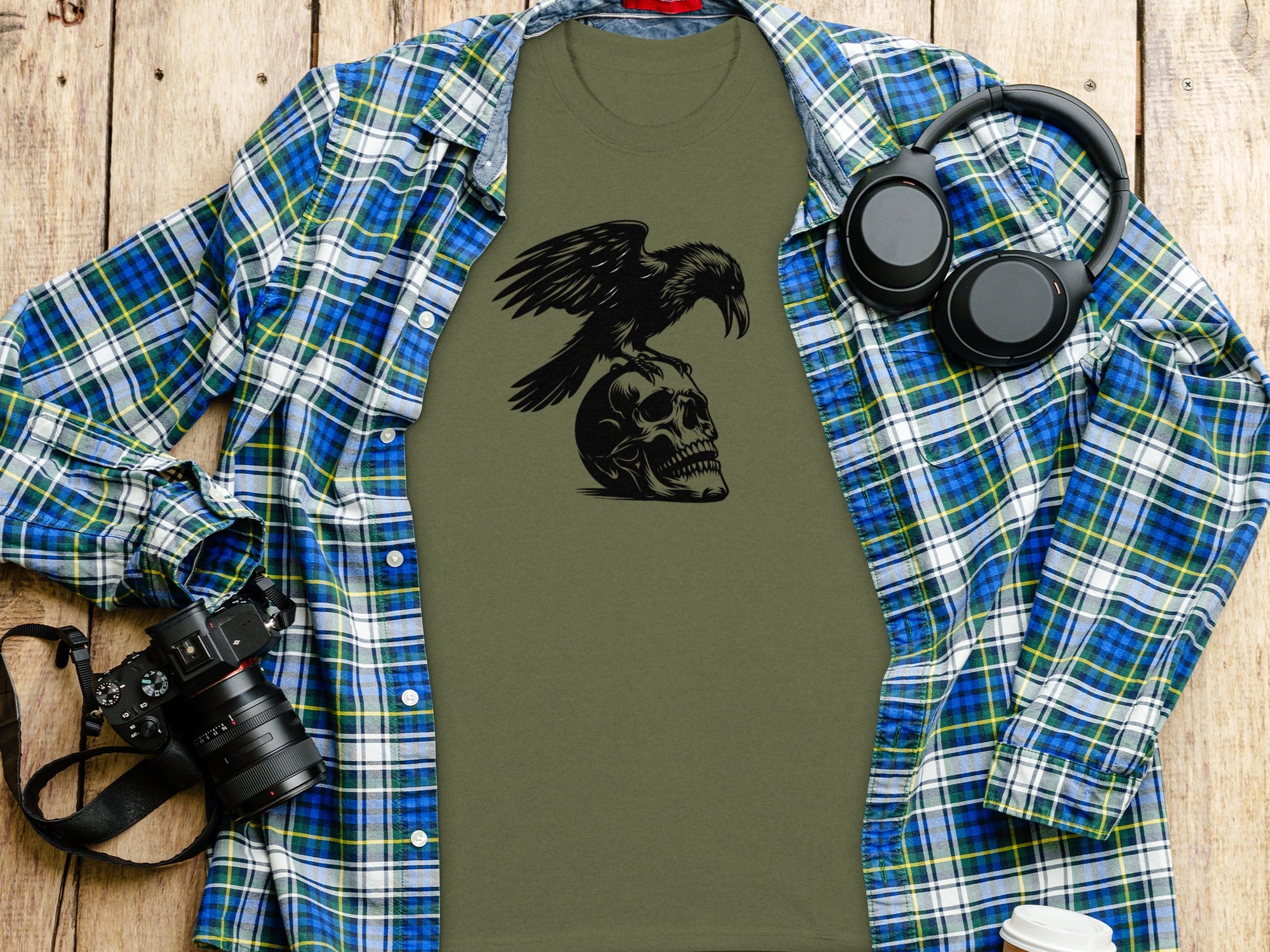 Green t-shirt with black raven on skull graphic, open plaid shirt, headphones and camera.