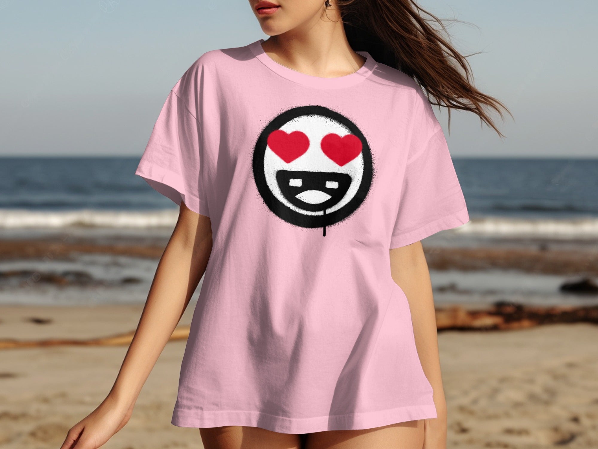 Pink t-shirt with a black circular logo featuring a smiling face with red heart eyes.