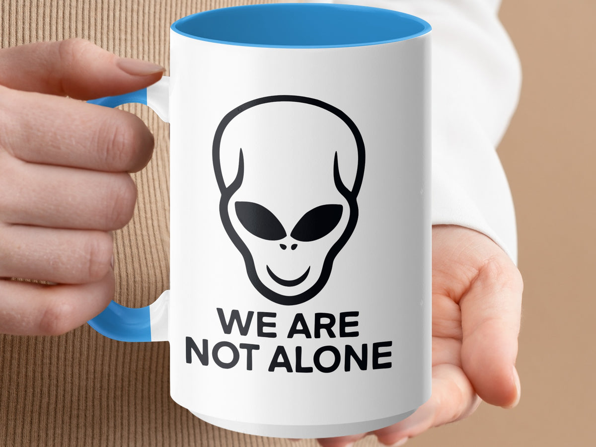 White mug with blue interior and handle, featuring a black alien head and "WE ARE NOT ALONE" text.