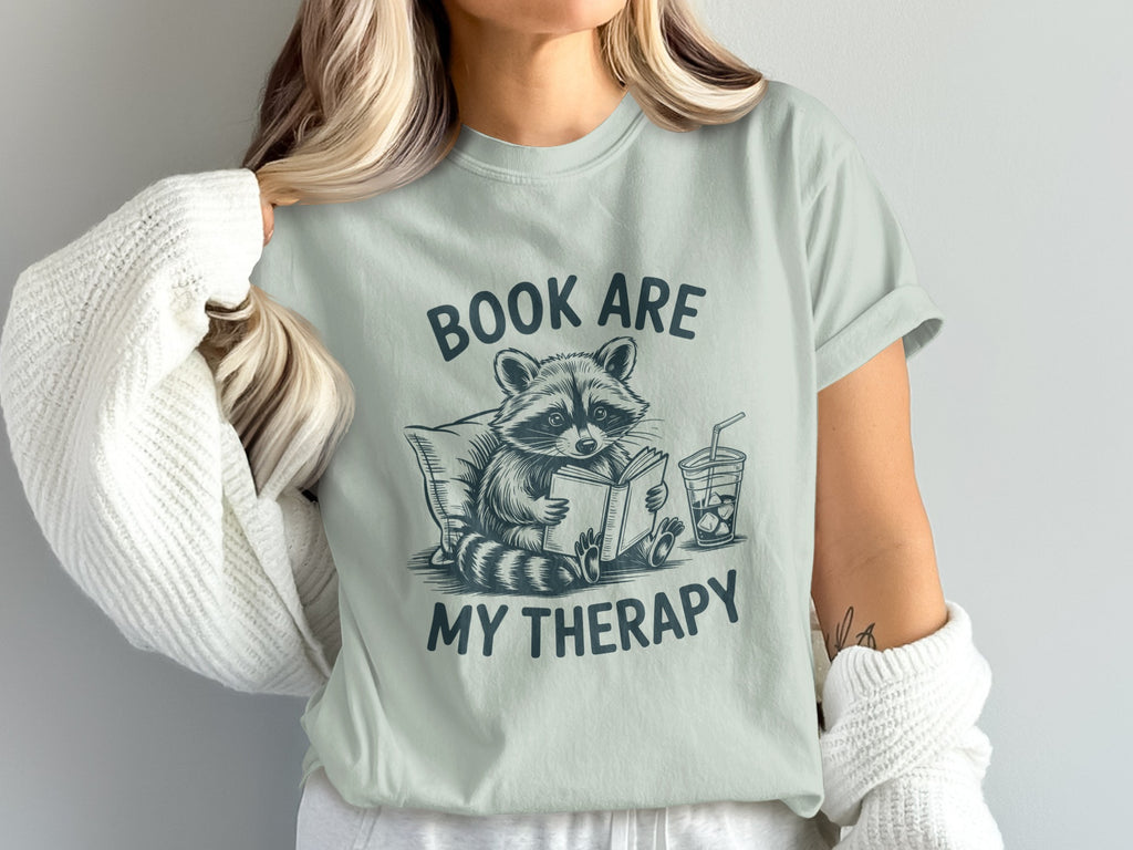 T-shirt graphic: raccoon reading book, "BOOK ARE MY THERAPY" text.