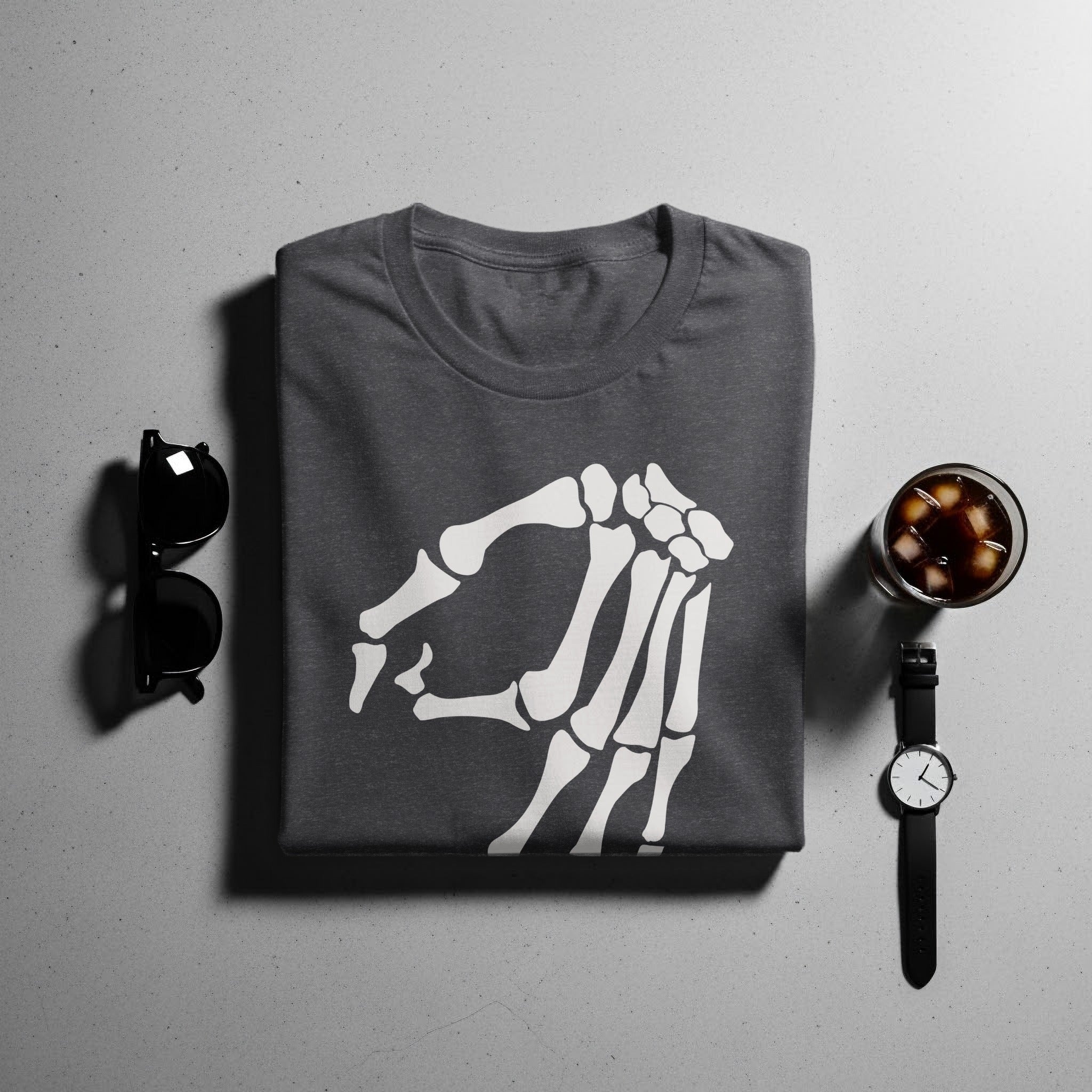 Dark grey t-shirt with a white skeleton hand graphic, displayed with sunglasses, watch and drink.