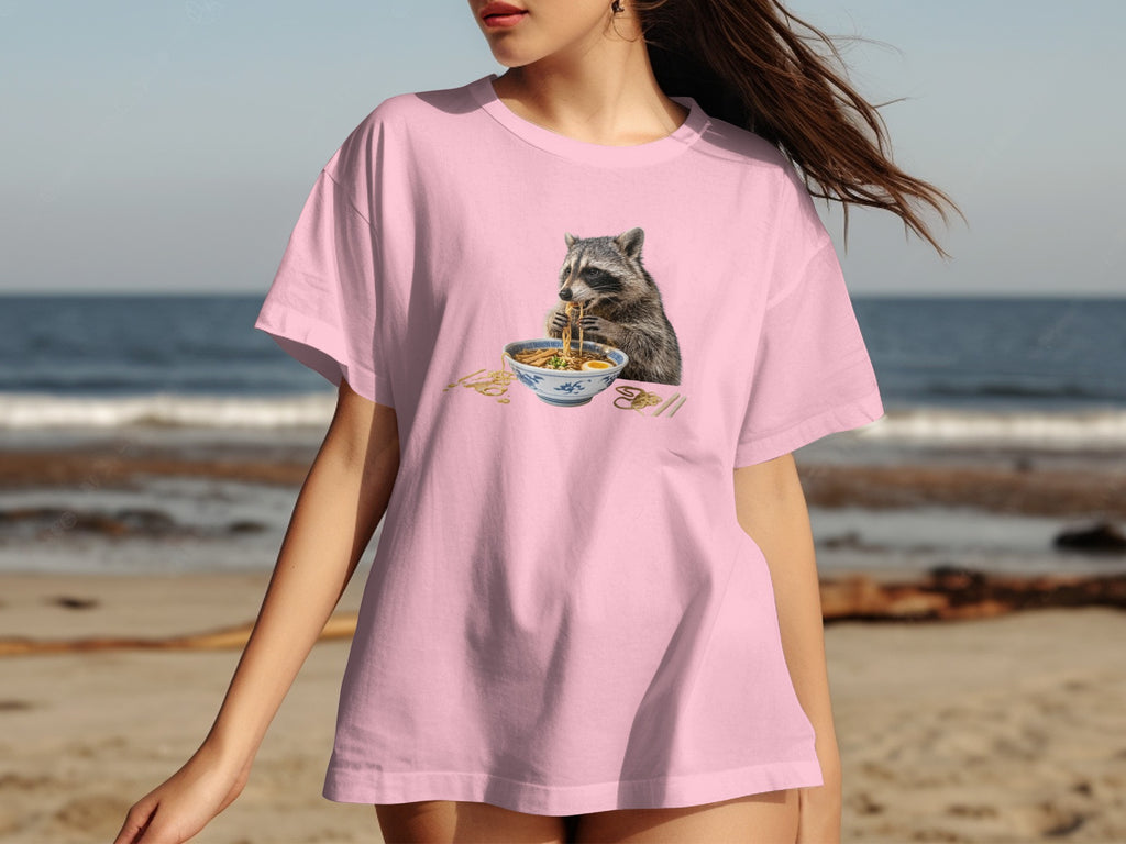 Pink t-shirt with a graphic of a raccoon eating ramen noodles.