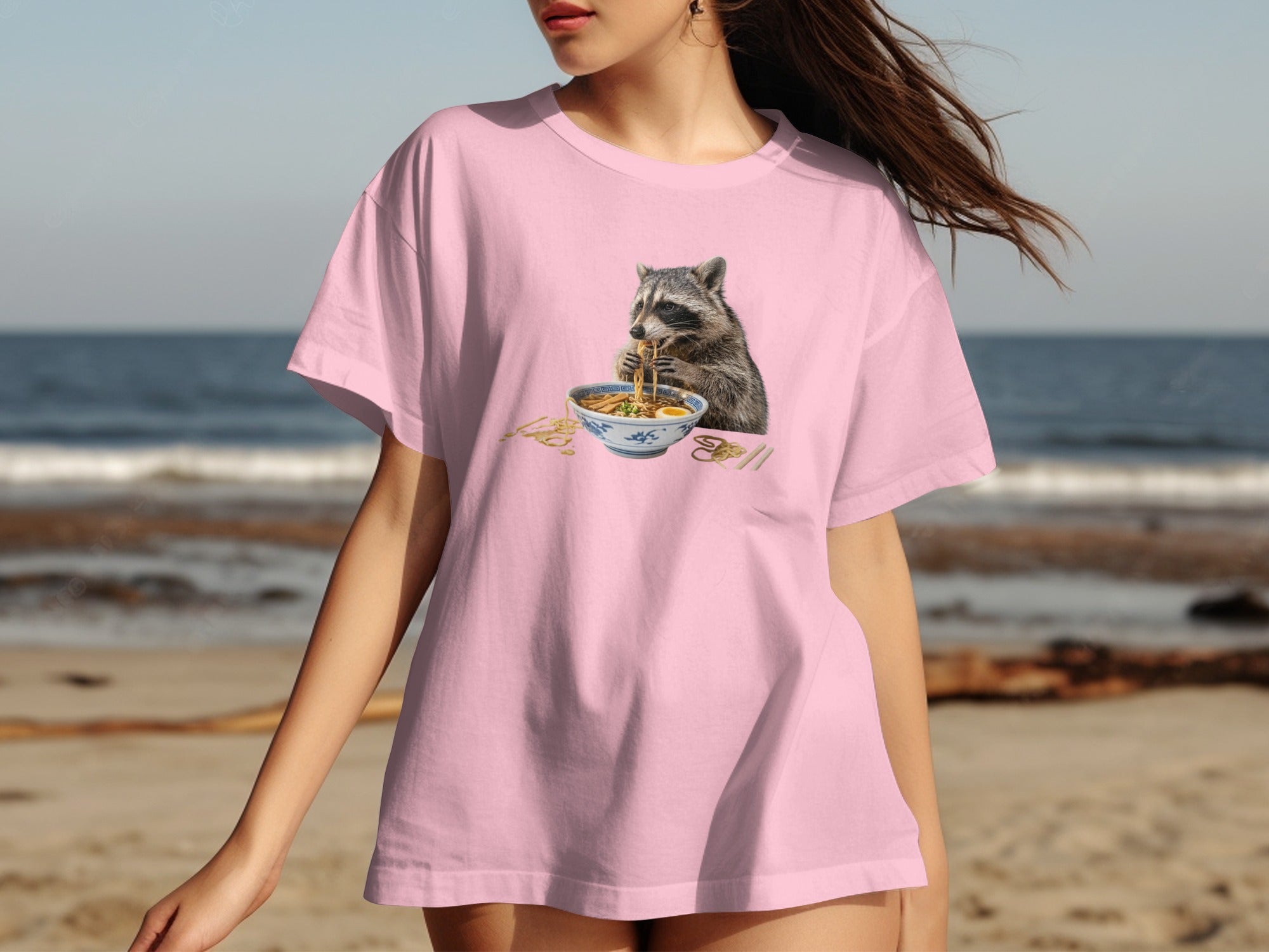 Pink t-shirt with a graphic of a raccoon eating ramen noodles.