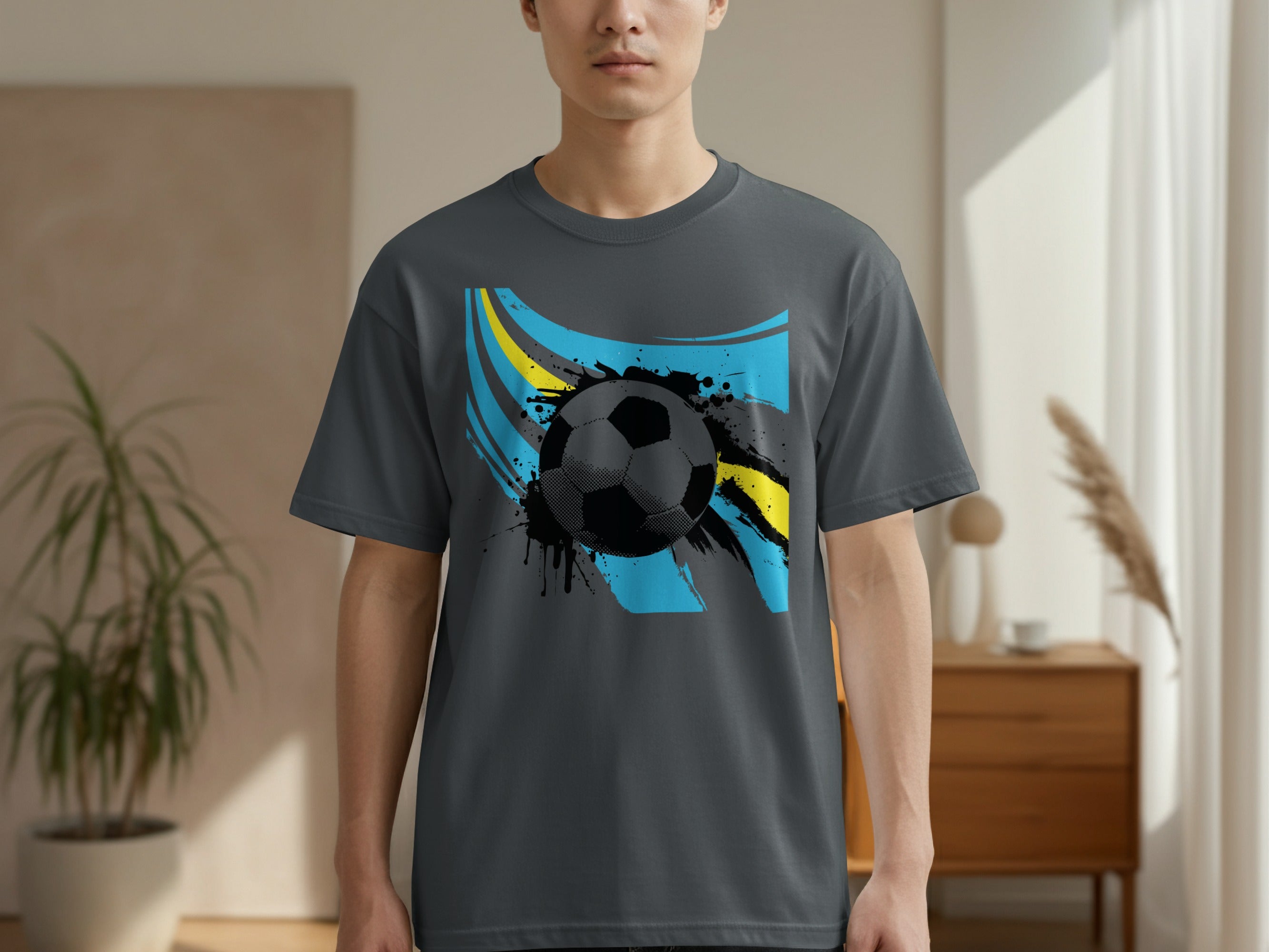 Grey t-shirt with black soccer ball on abstract blue and yellow background.