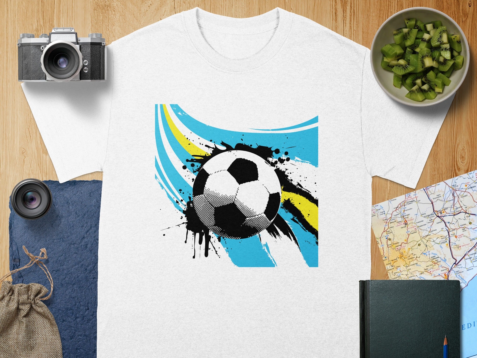 White t-shirt with abstract soccer ball graphic and blue and yellow brush strokes.