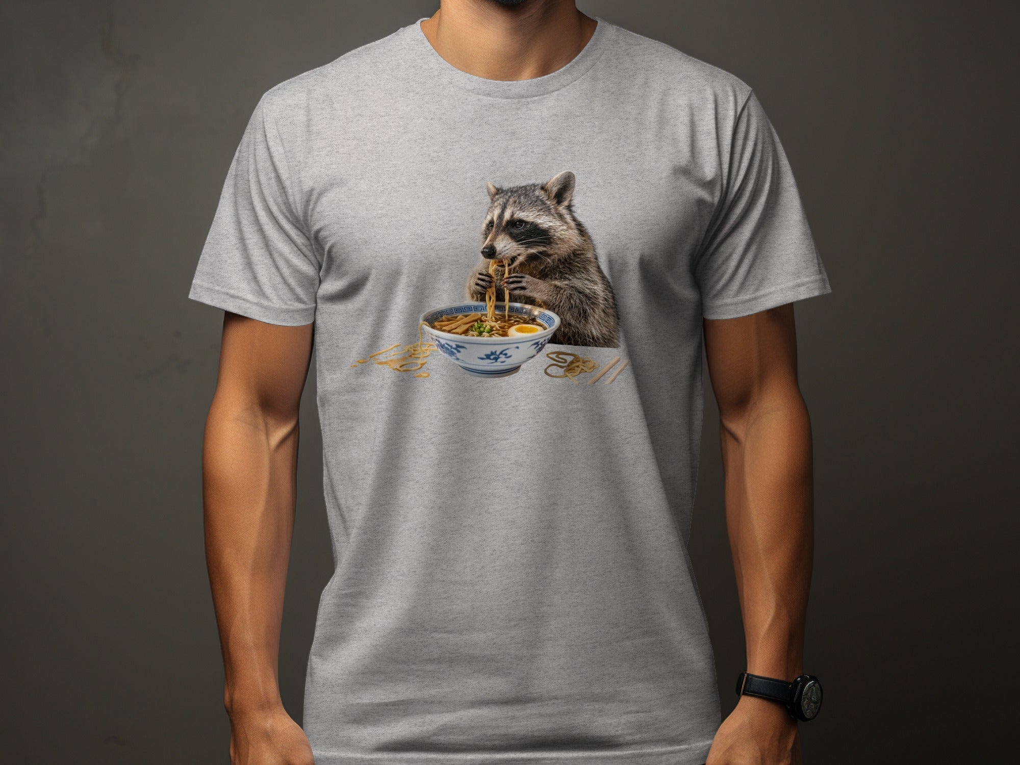 Raccoon eating ramen noodles from a bowl on a gray t-shirt.