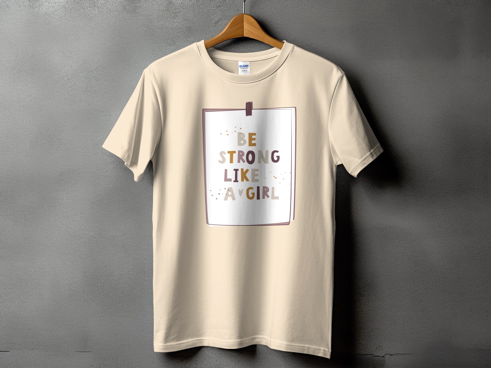 Light tan t-shirt with text "BE STRONG LIKE A GIRL" in a box.
