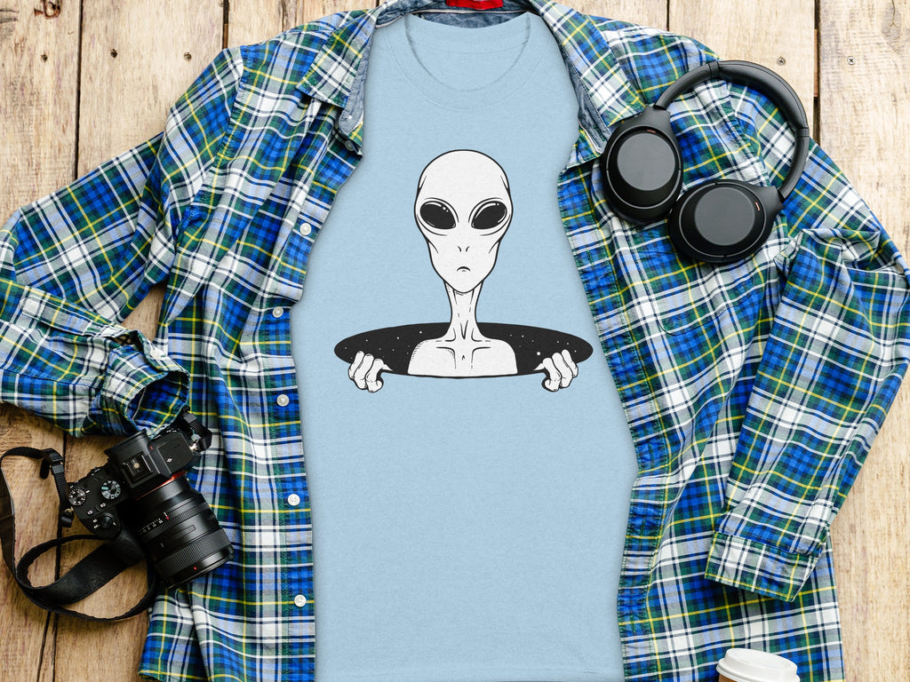 Light blue t-shirt with alien graphic, open plaid shirt, headphones, and camera.