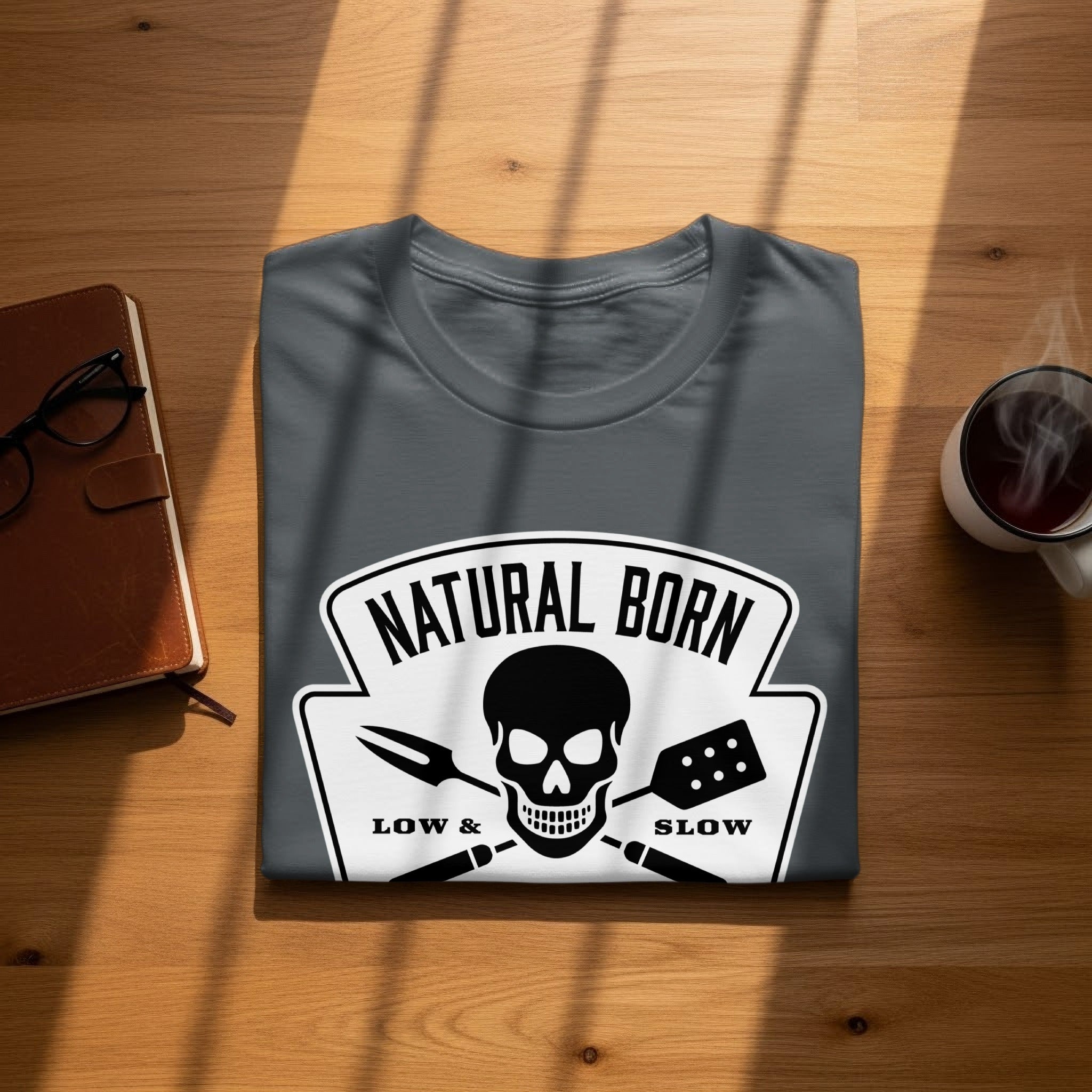 Dark grey t-shirt with a skull, spatula, and fork design that reads "NATURAL BORN LOW & SLOW".