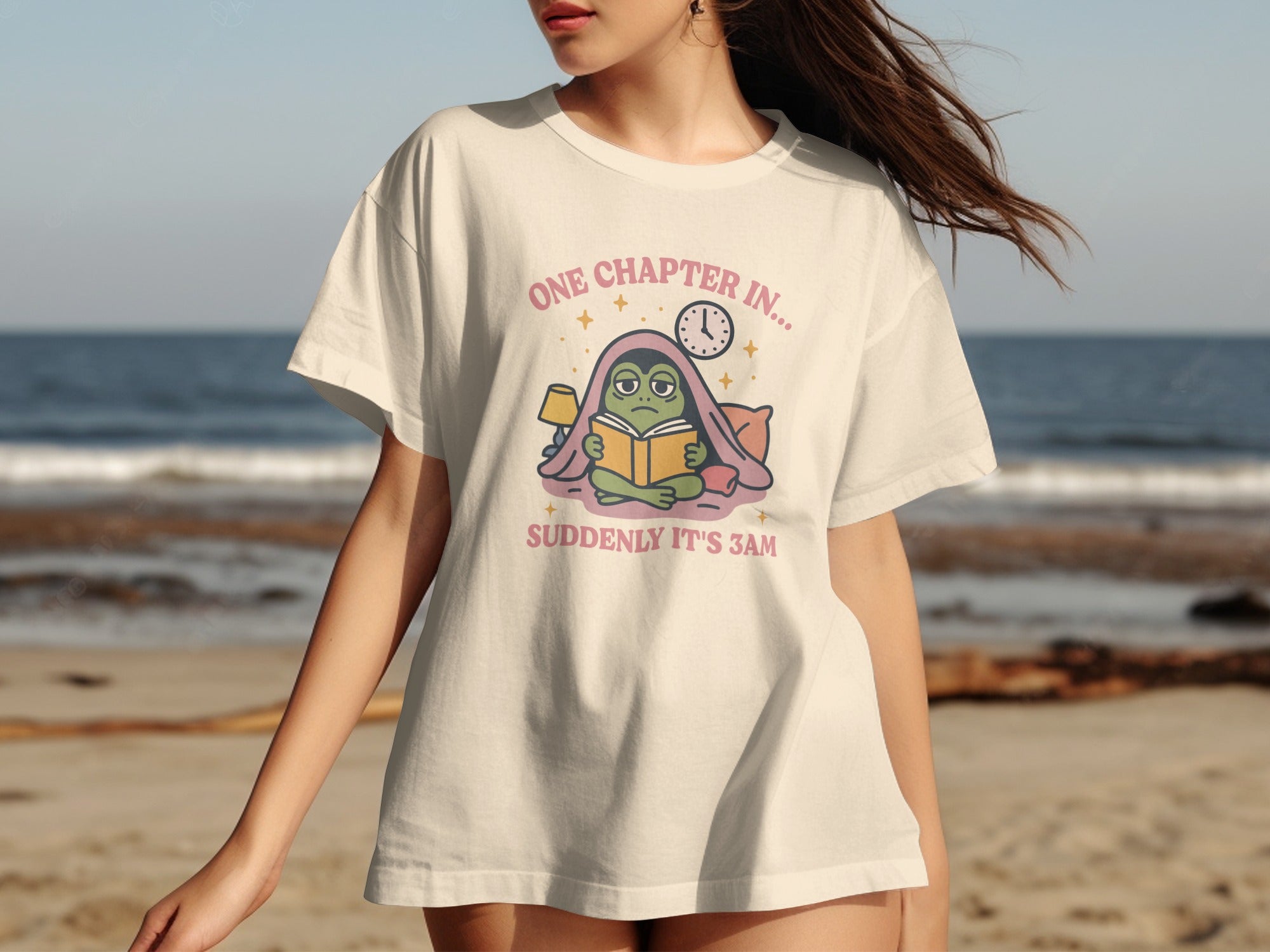 T-shirt graphic: A frog reads under covers, text reads "One chapter in... Suddenly it's 3am".