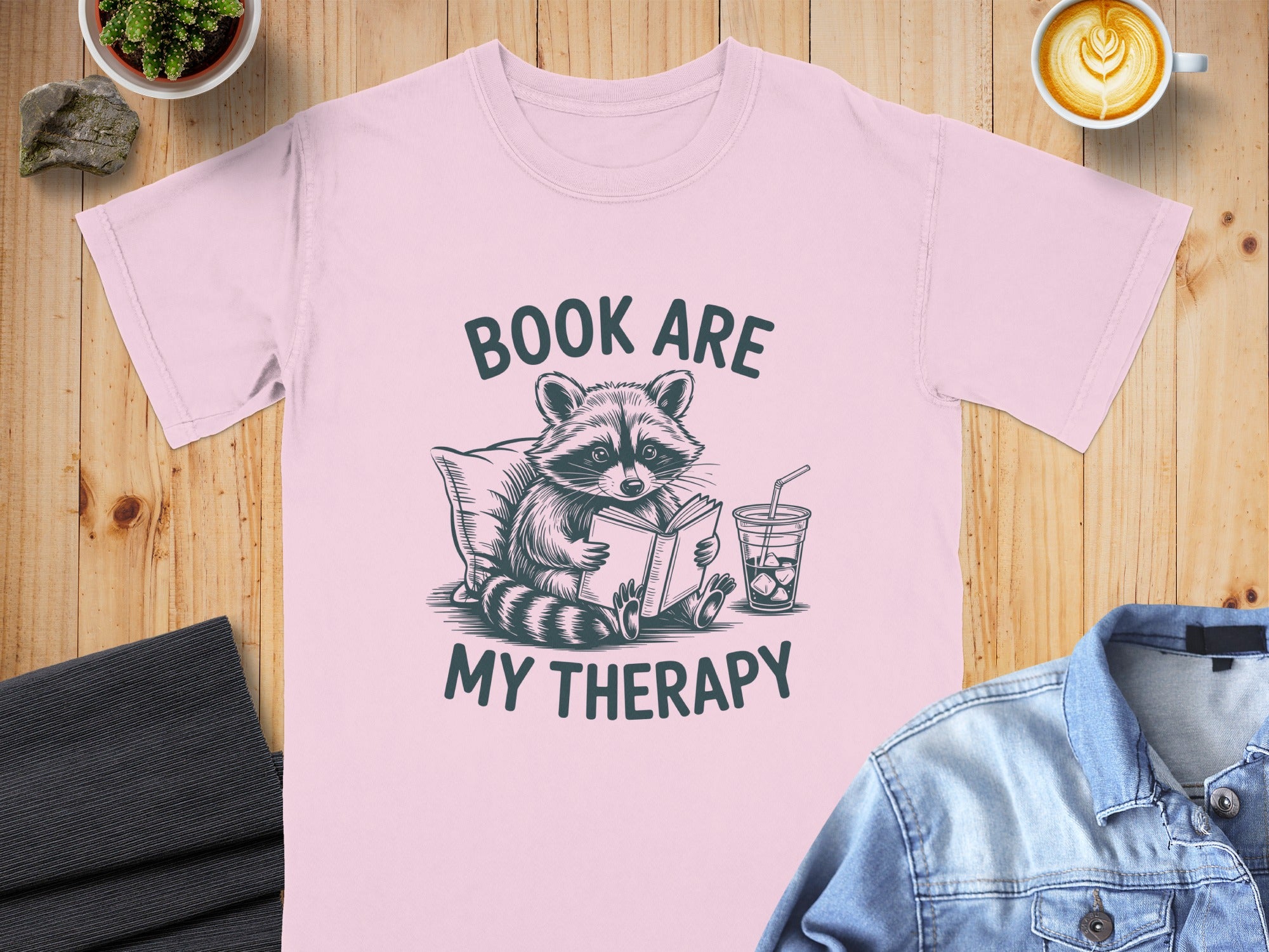 Pink t-shirt with raccoon reading a book and text "BOOK ARE MY THERAPY".