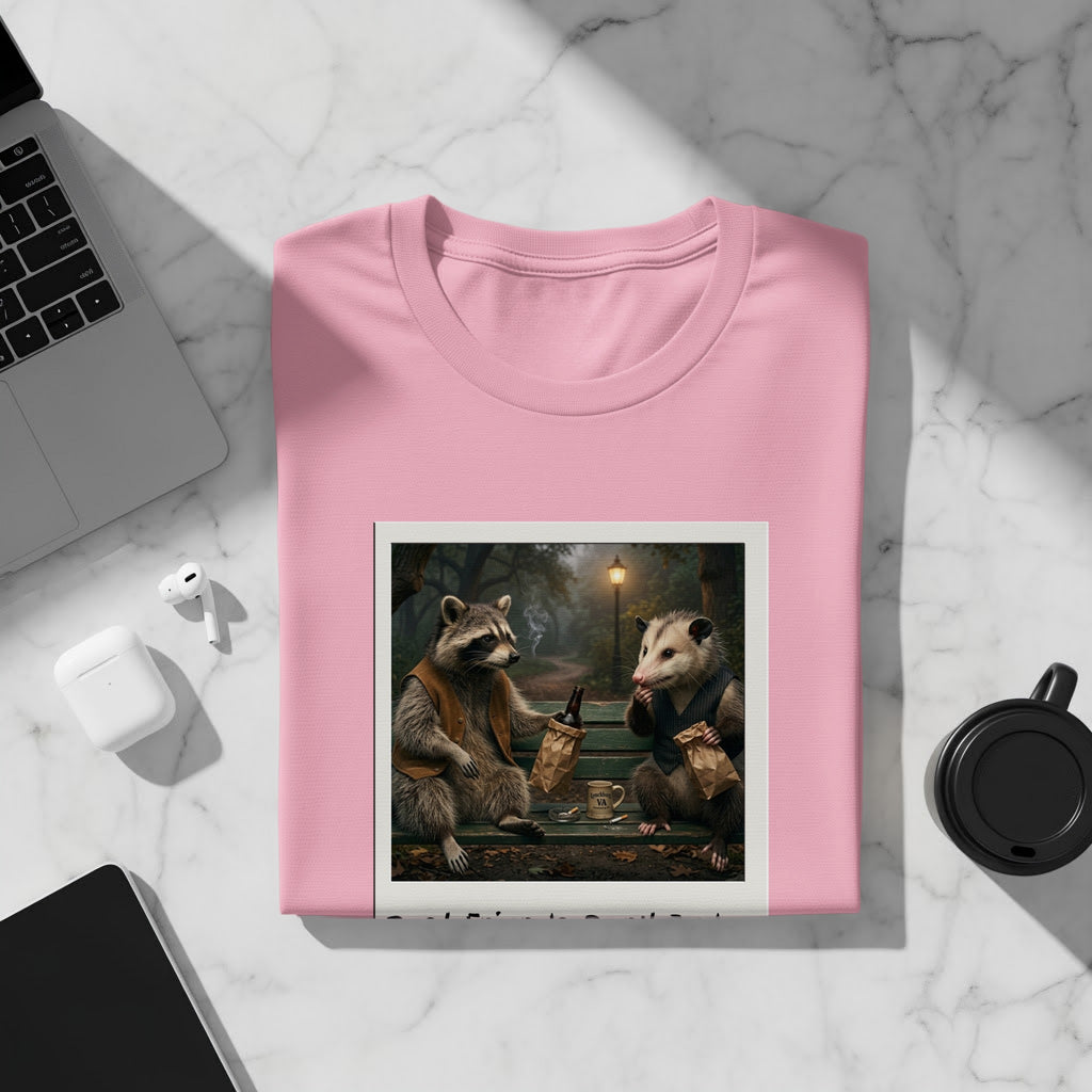 Pink t-shirt with graphic of raccoon and possum sharing drinks on a bench.