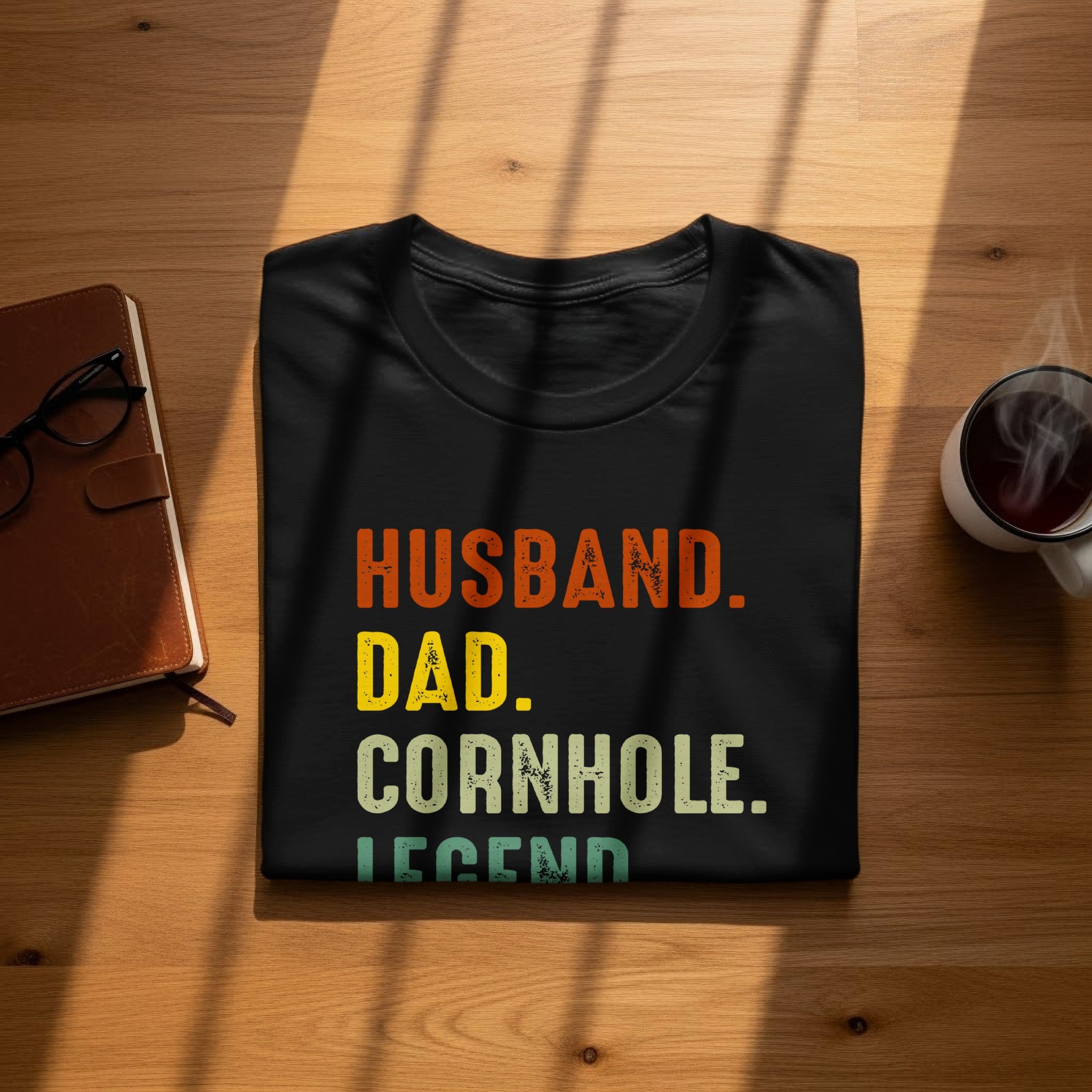 Black t-shirt with text "Husband. Dad. Cornhole. Legend." on a wooden surface.