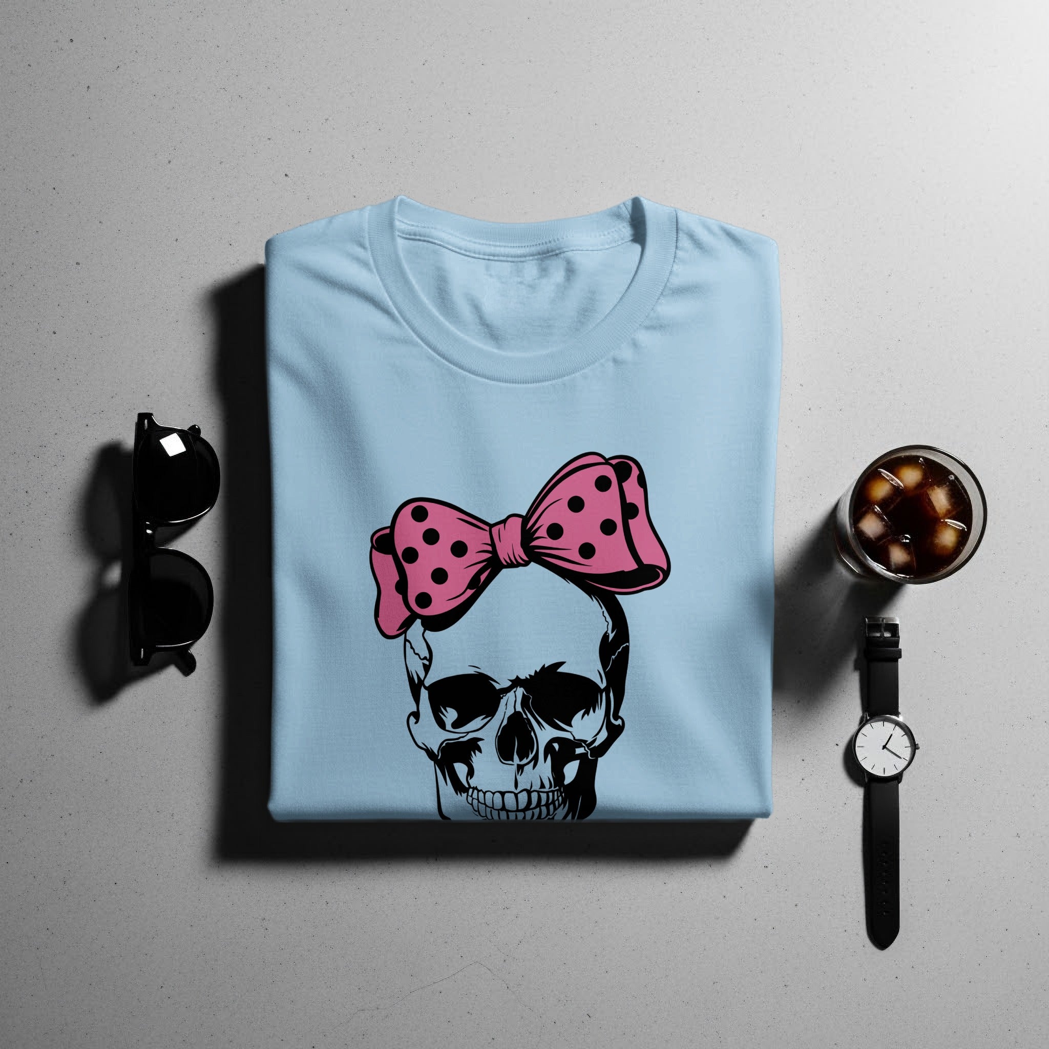 Light blue t-shirt with a black skull graphic wearing a pink polka dot bow.