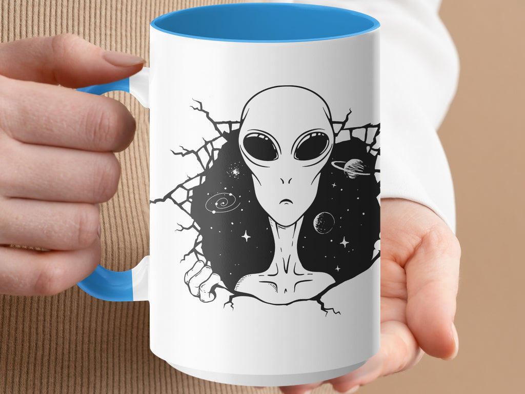 White mug with blue handle and interior, featuring a black alien emerging from a cracked space background.