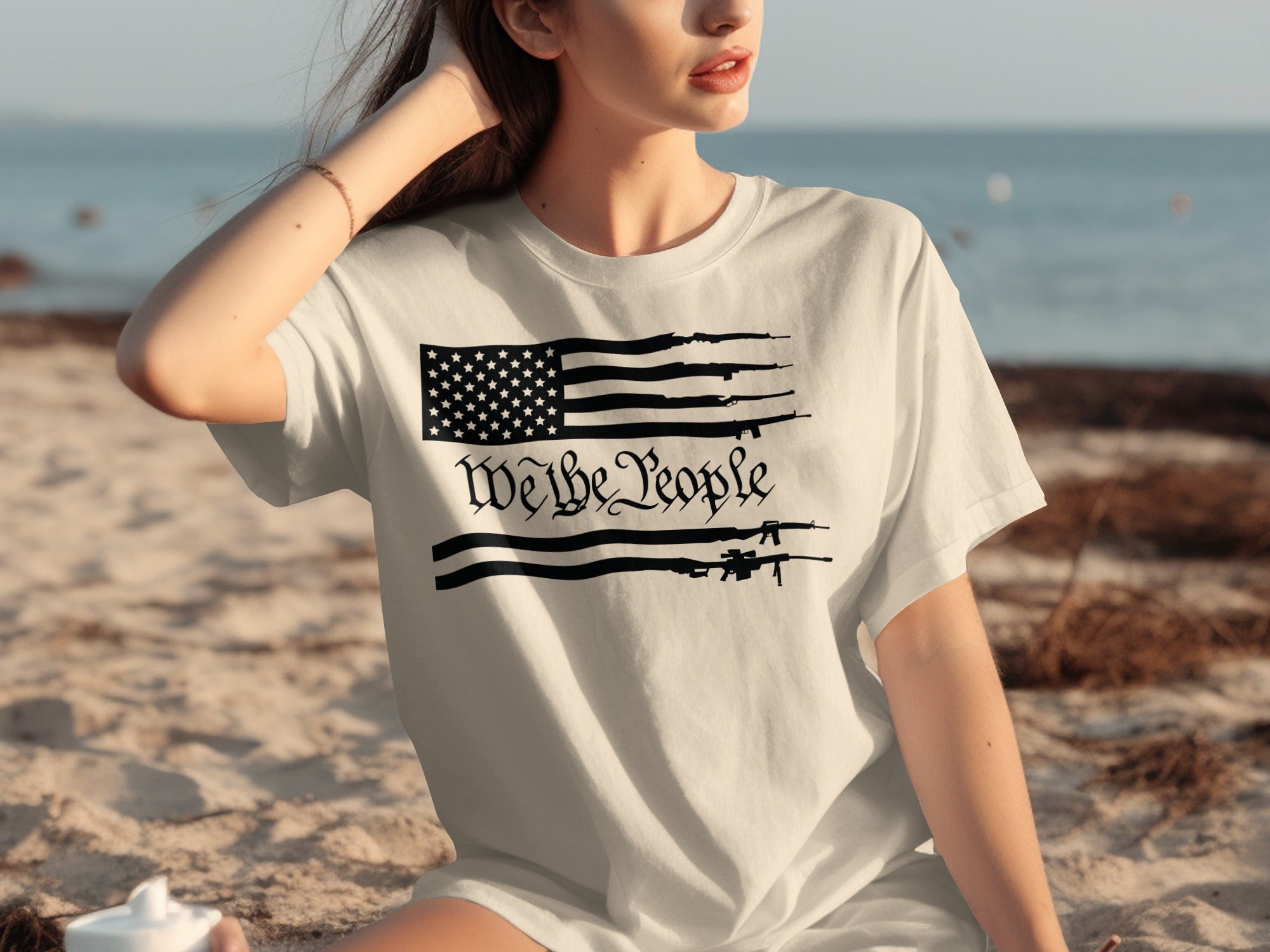 White t-shirt with black American flag design incorporating guns and text "We the People".