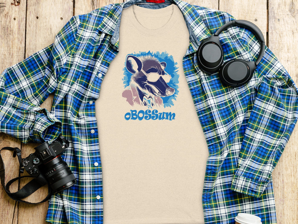 Beige t-shirt with sunglasses-wearing opossum graphic and "cBOSSum" text alongside plaid shirt.