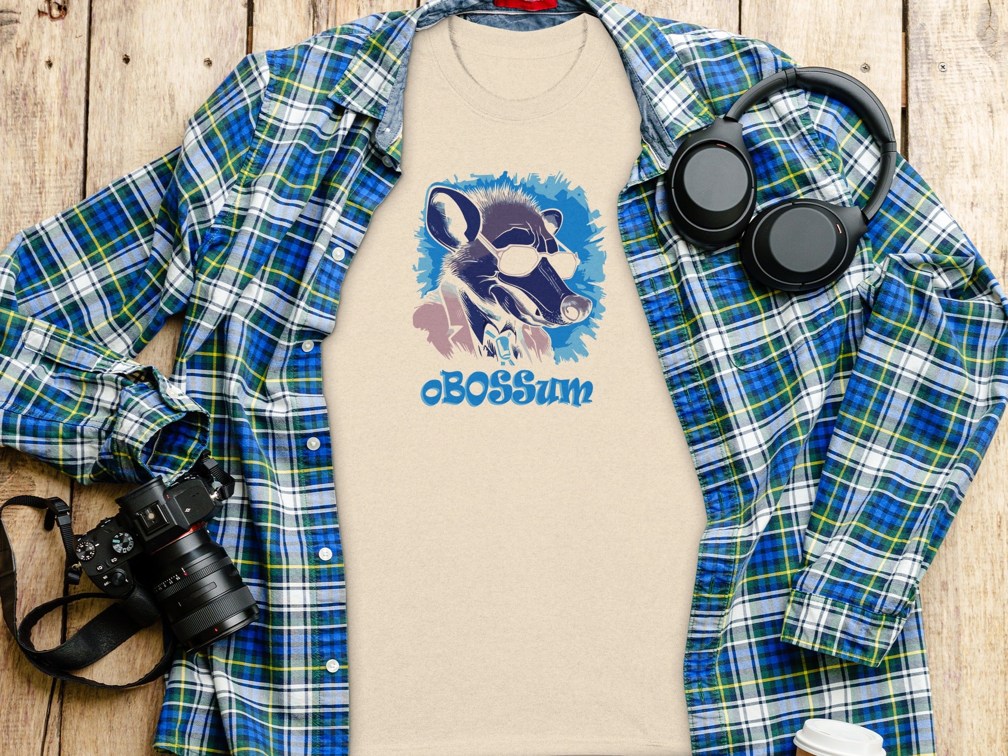 Beige t-shirt with sunglasses-wearing opossum graphic and "cBOSSum" text alongside plaid shirt.