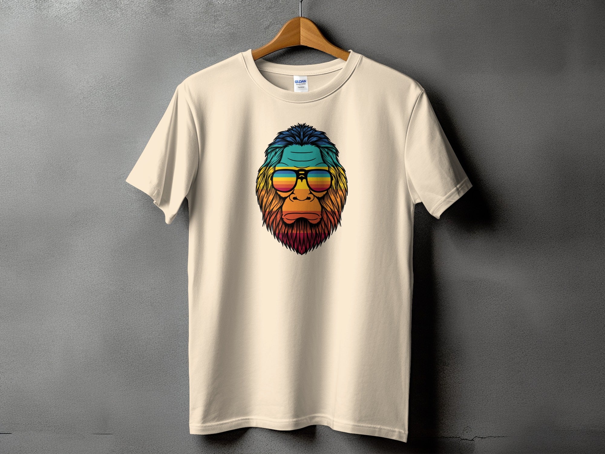 Cream t-shirt featuring a colorful, retro Bigfoot graphic with striped sunglasses.