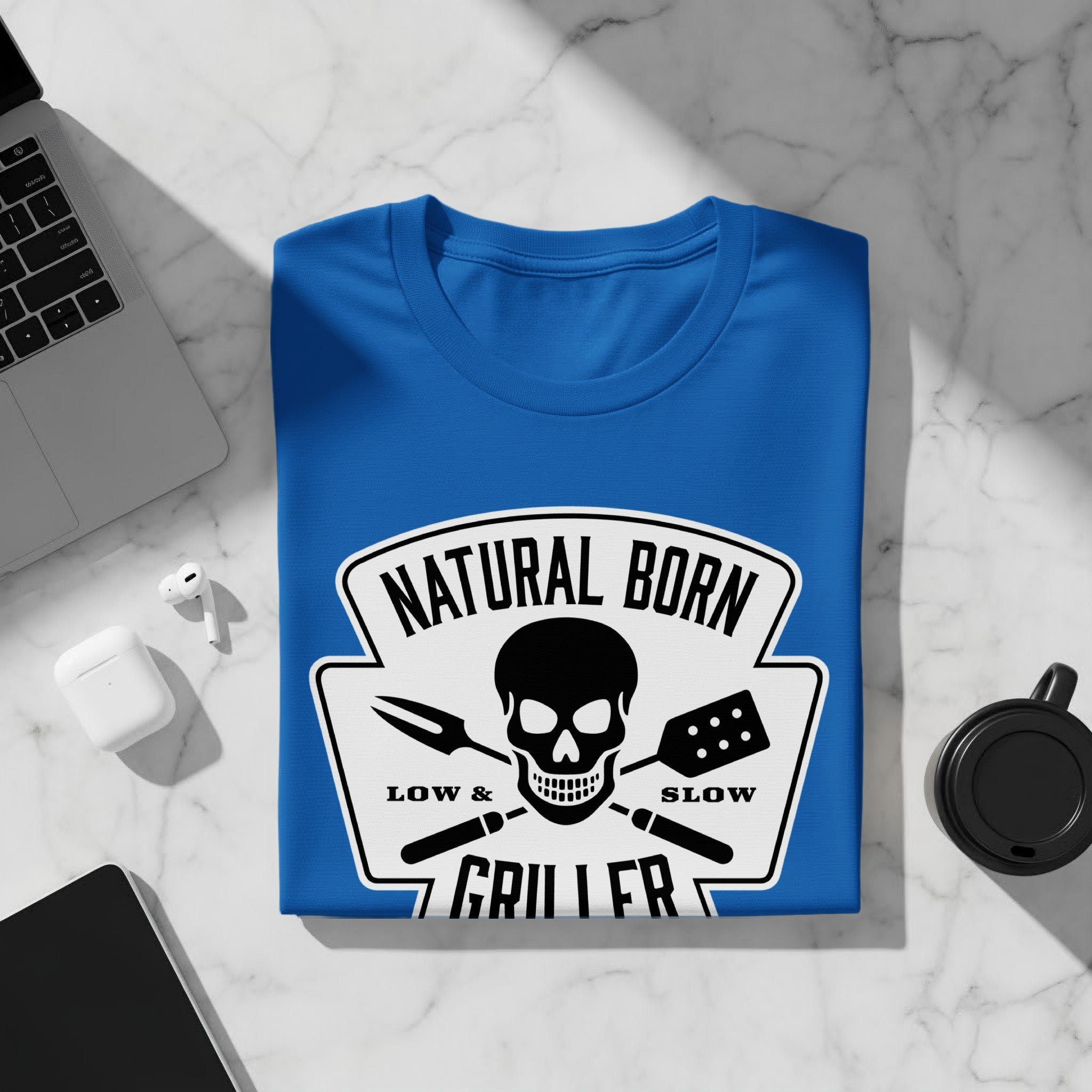 Blue t-shirt with "Natural Born Griller" text, skull, fork, and spatula graphic.