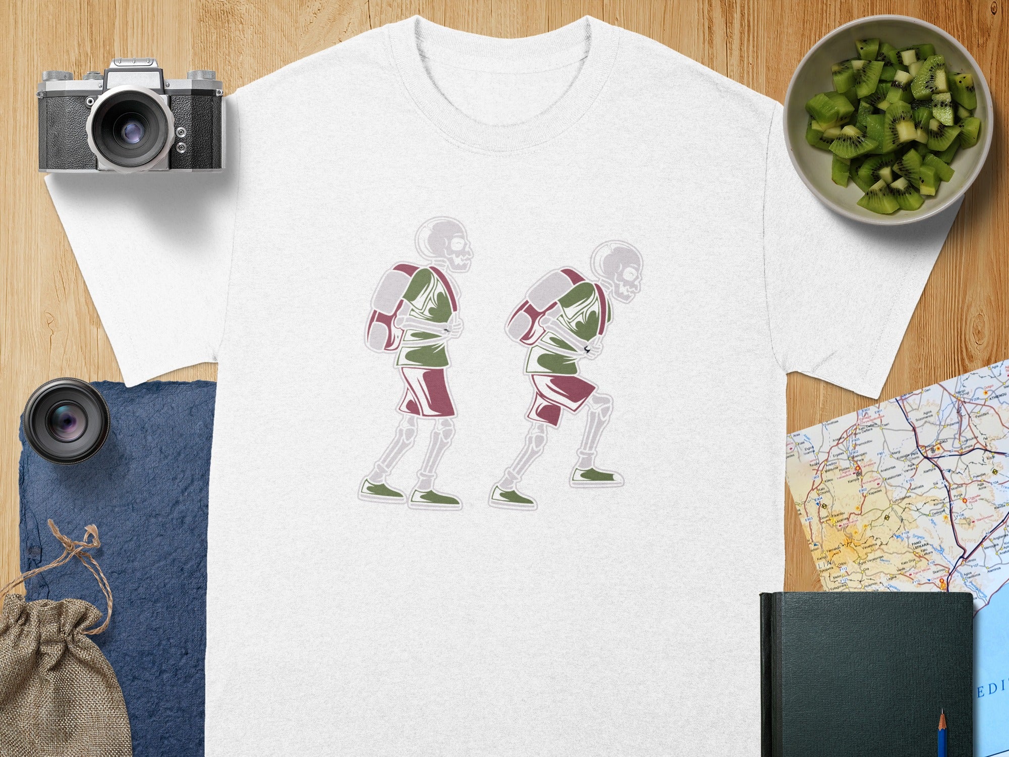 White t-shirt with two skeletons wearing backpacks and shorts, walking to the right.