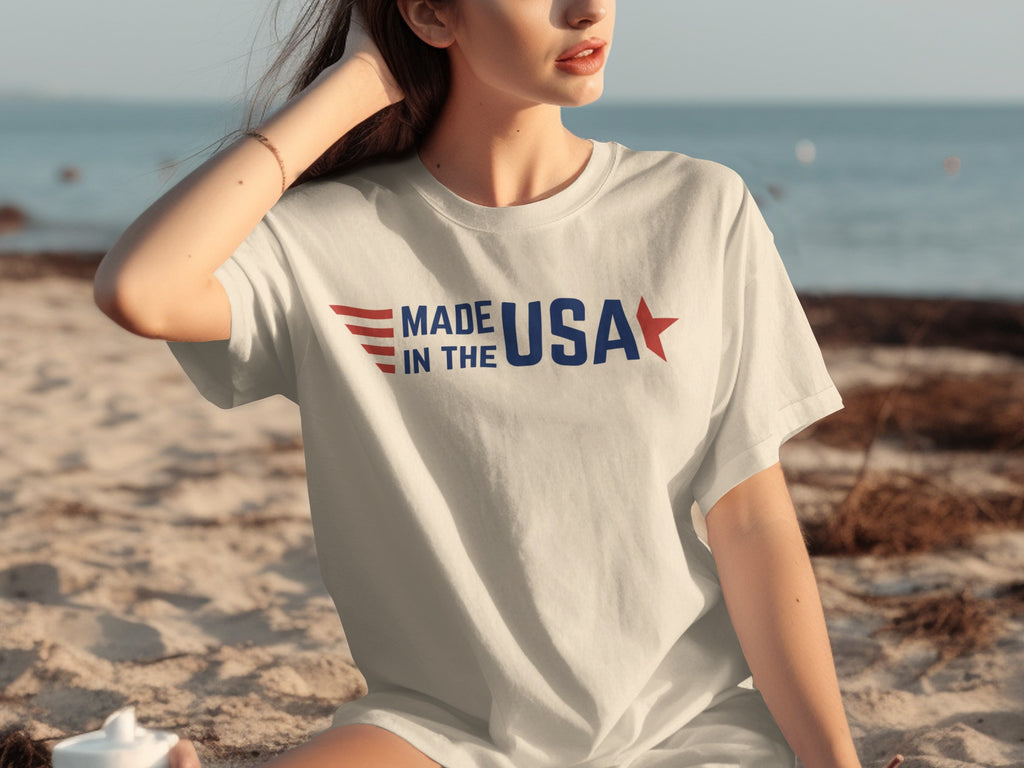 White t-shirt with "MADE IN THE USA" text and stars graphic on the beach.