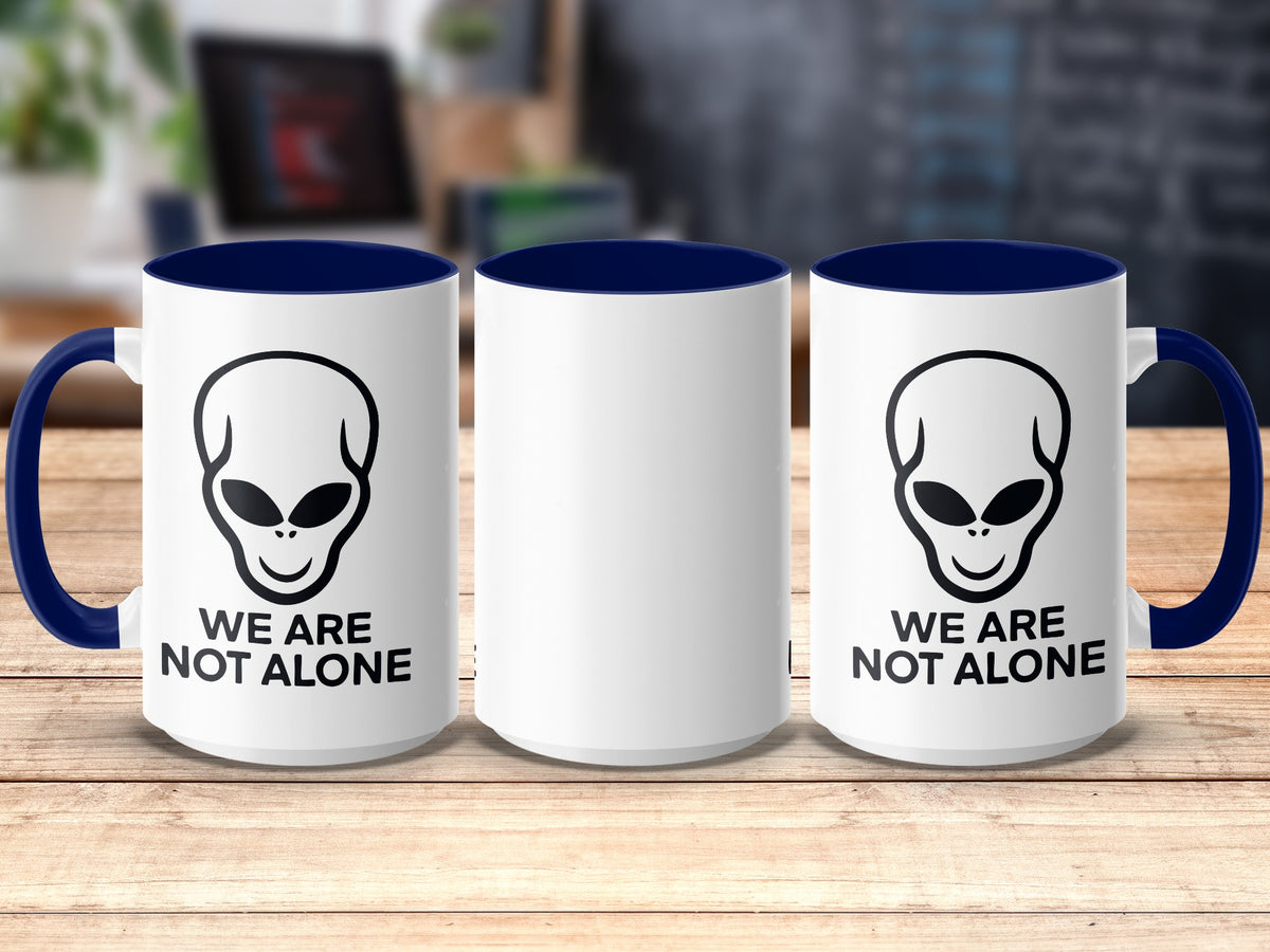 White mugs with blue handles and interiors, featuring alien heads and "We Are Not Alone" text.